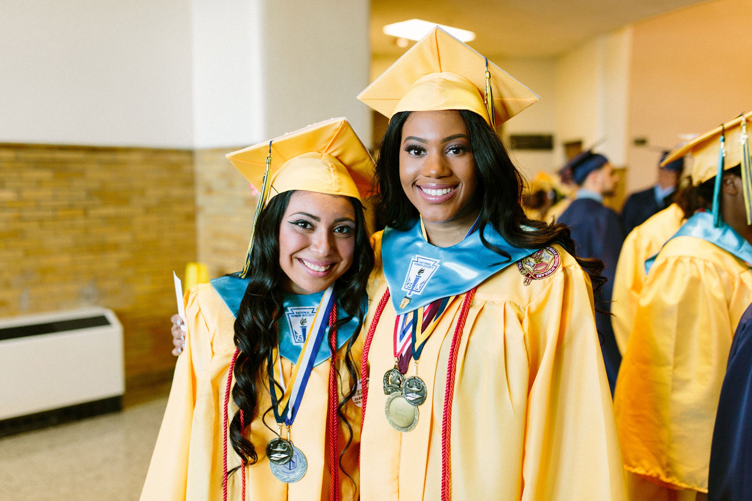 Two students wearing graduation caps and gowns embrace