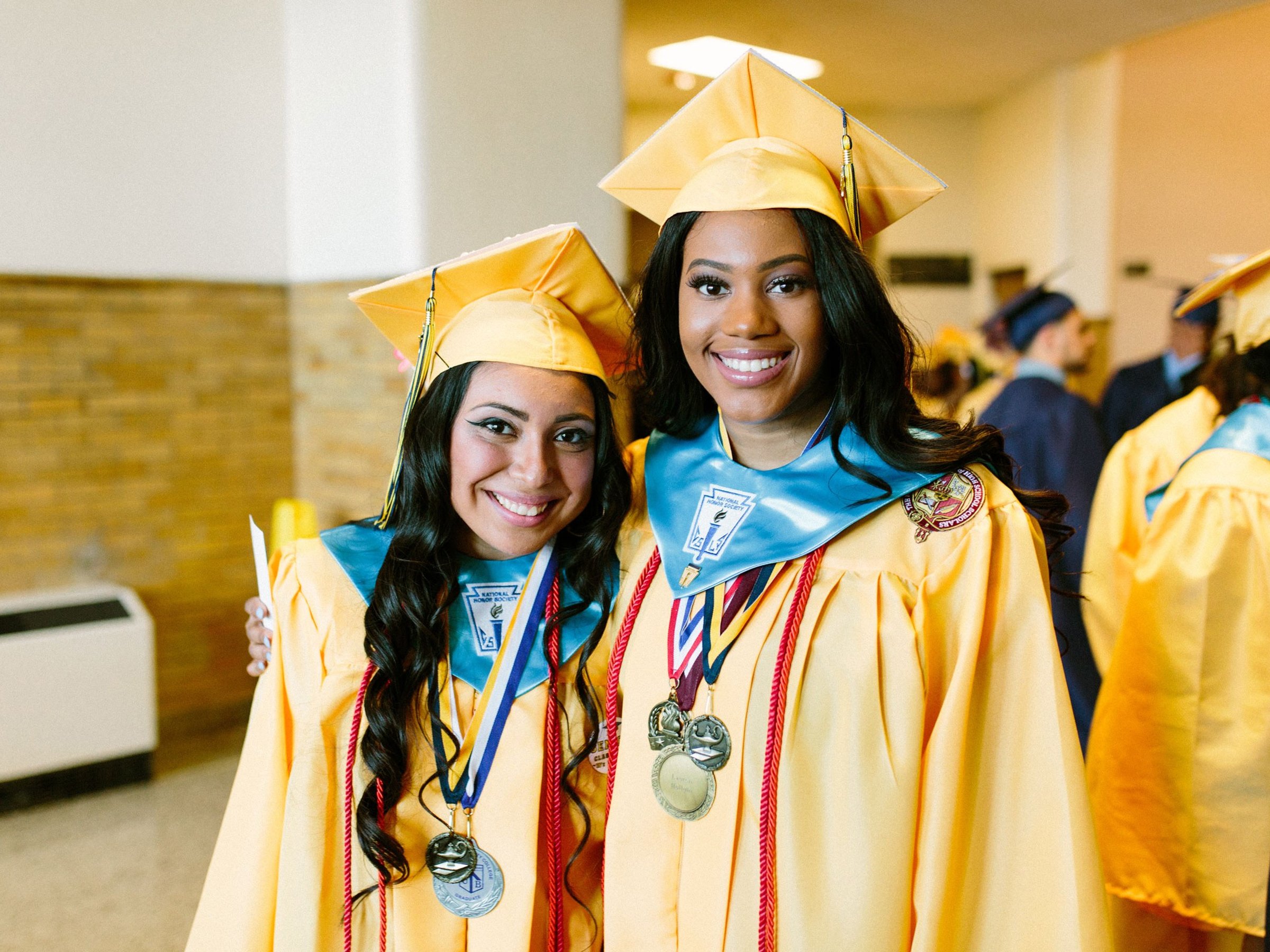 Two students wearing graduation caps and gowns embrace