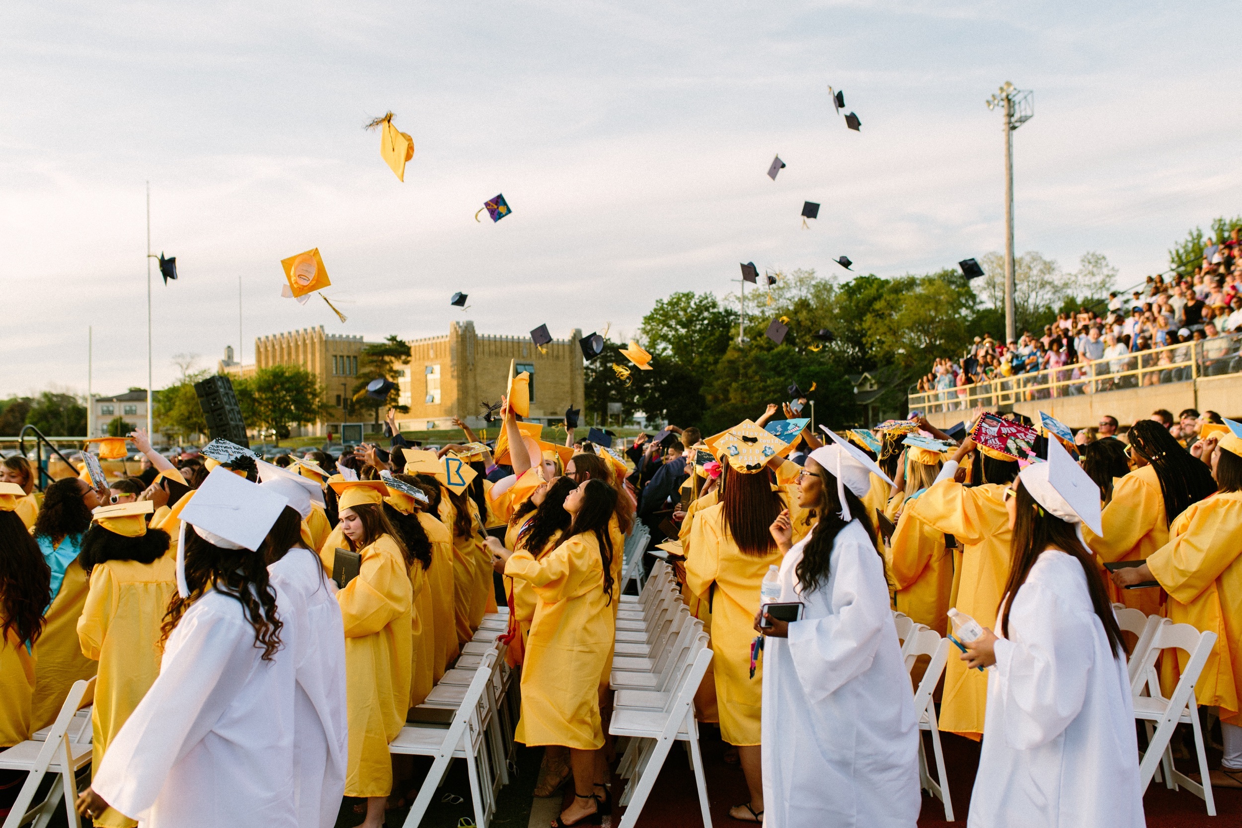 Graduation ceremony with students in yellow and white cap and gown, throwing caps into the air in celebration.
