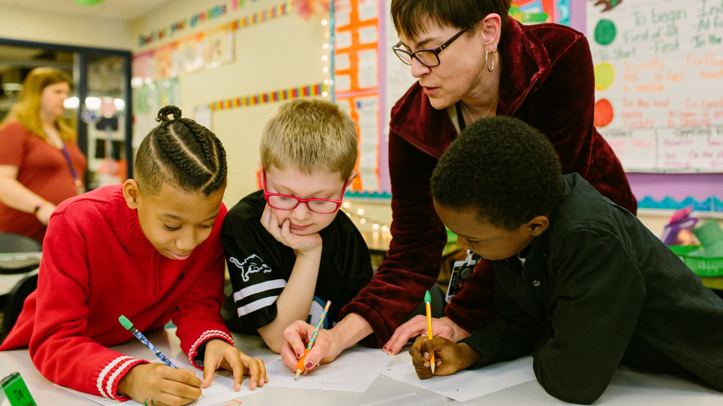 Three students writing with teacher helping