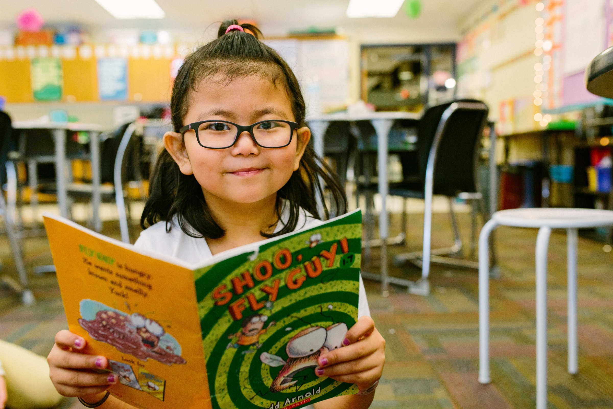 girl with glasses smiling while reading book