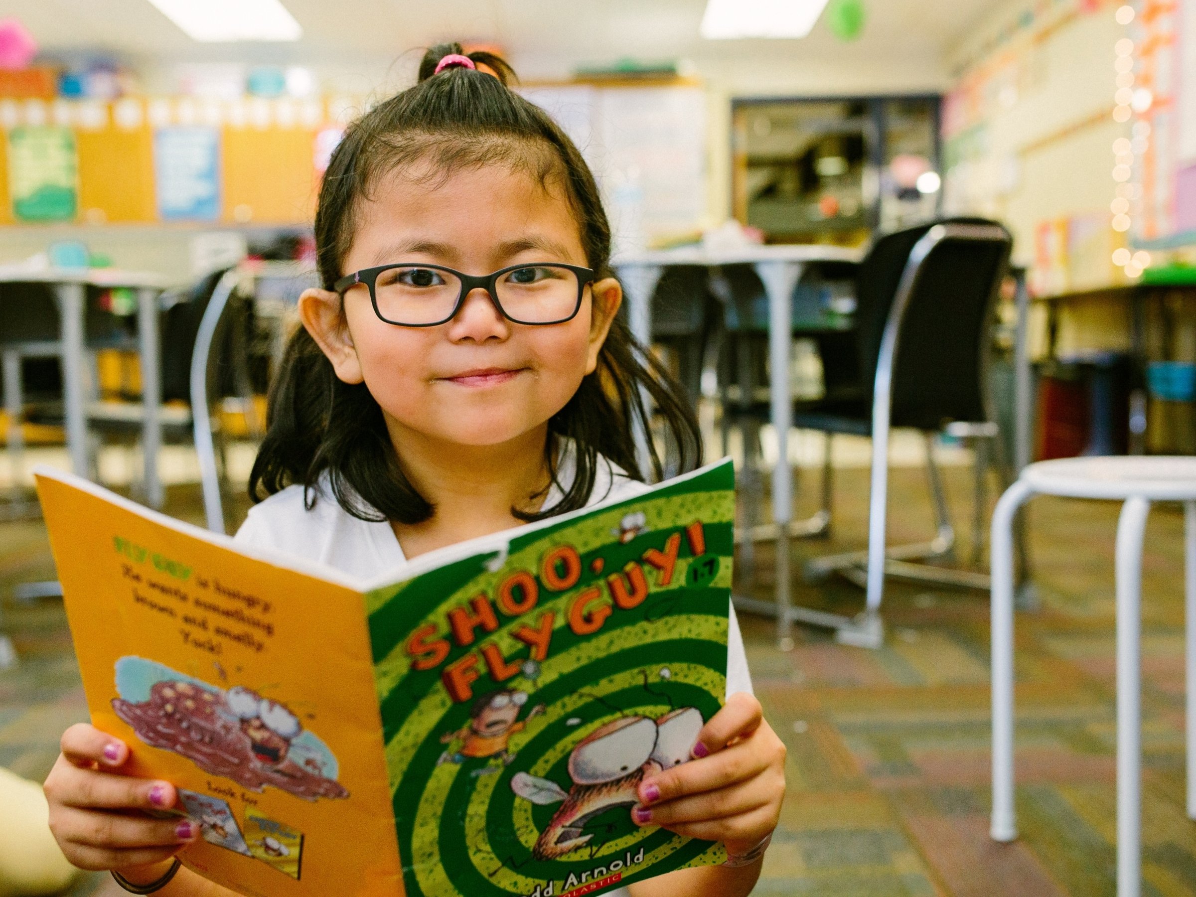 girl with glasses smiling while reading book