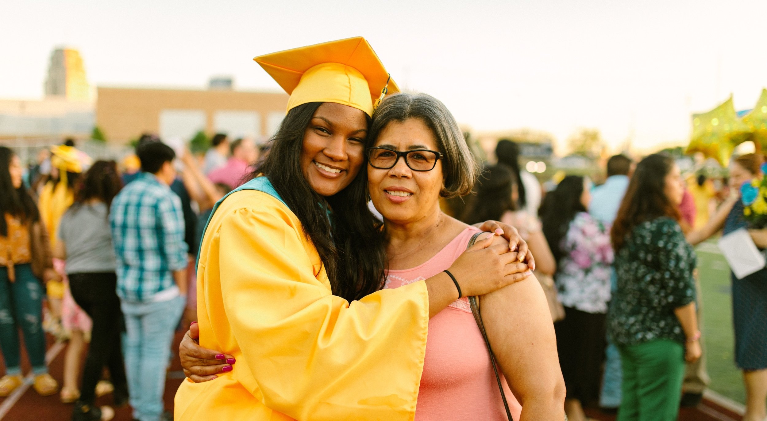 A graduating senior in cap and gown hugs a parent at the ceremony