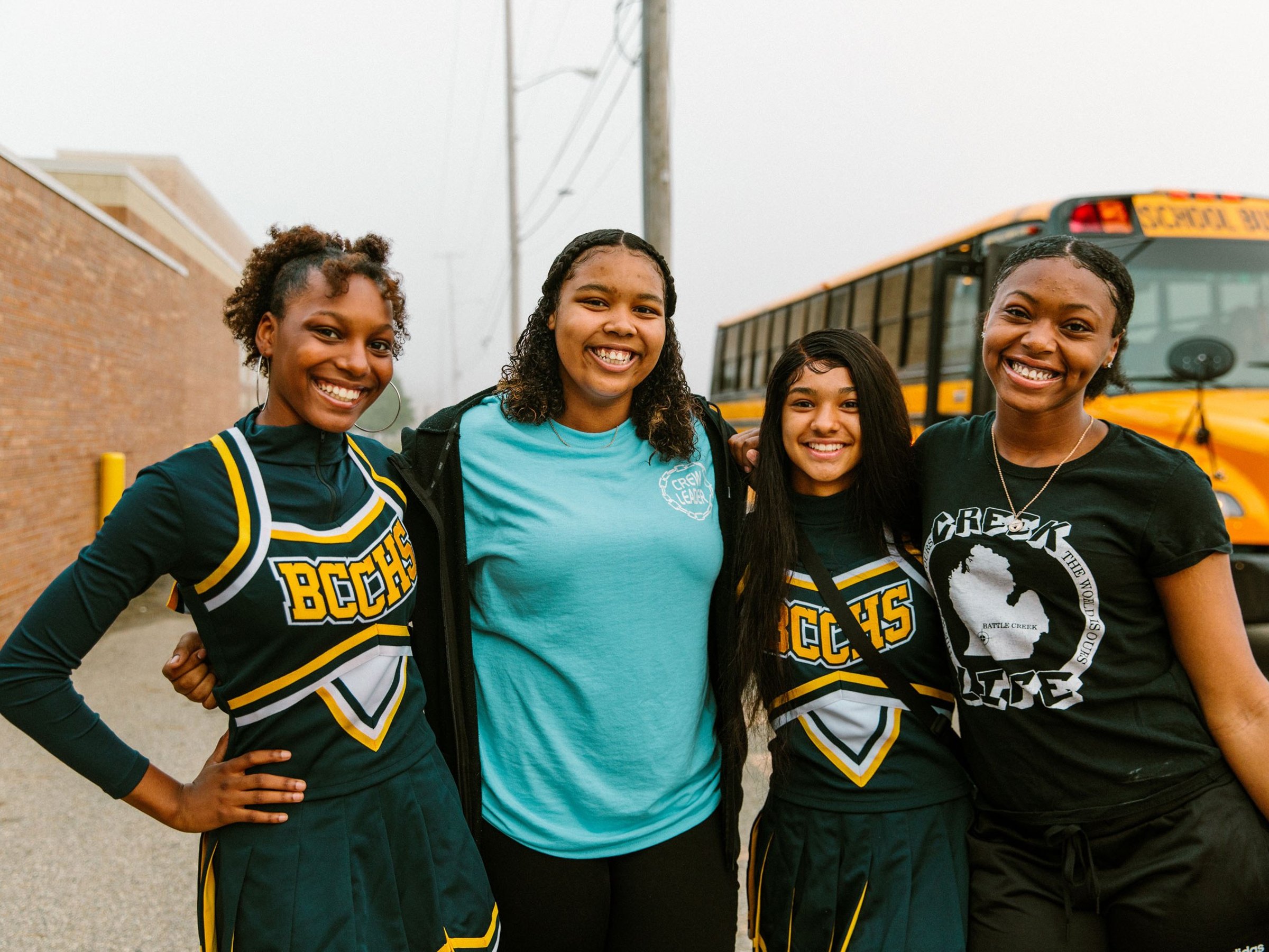 Four students smiling in front of a school bus