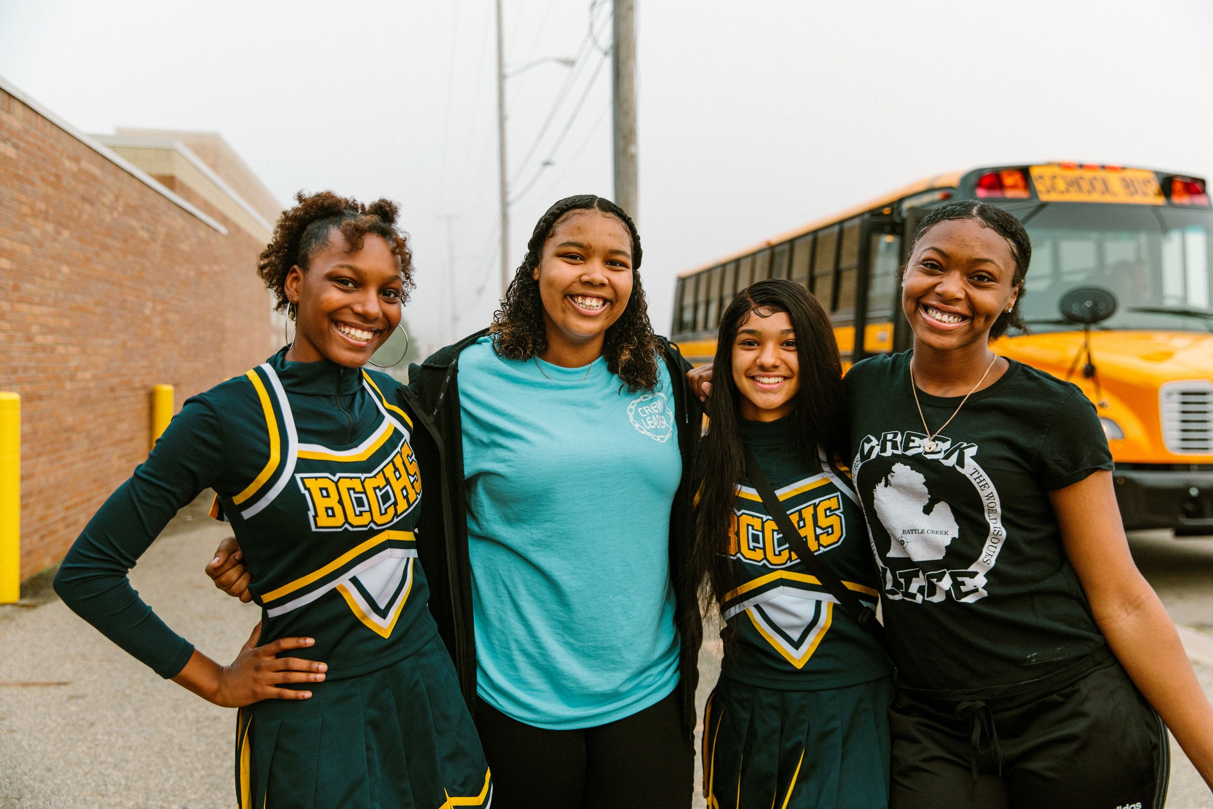 Four students smiling in front of a school bus