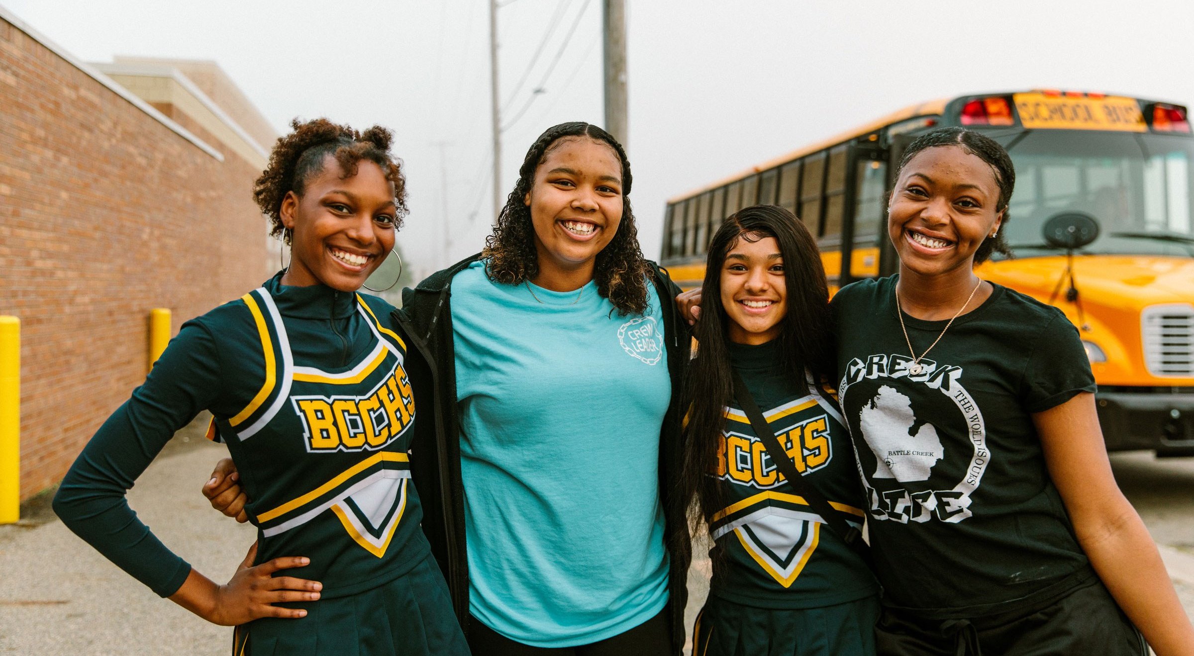 Four students smiling in front of a school bus
