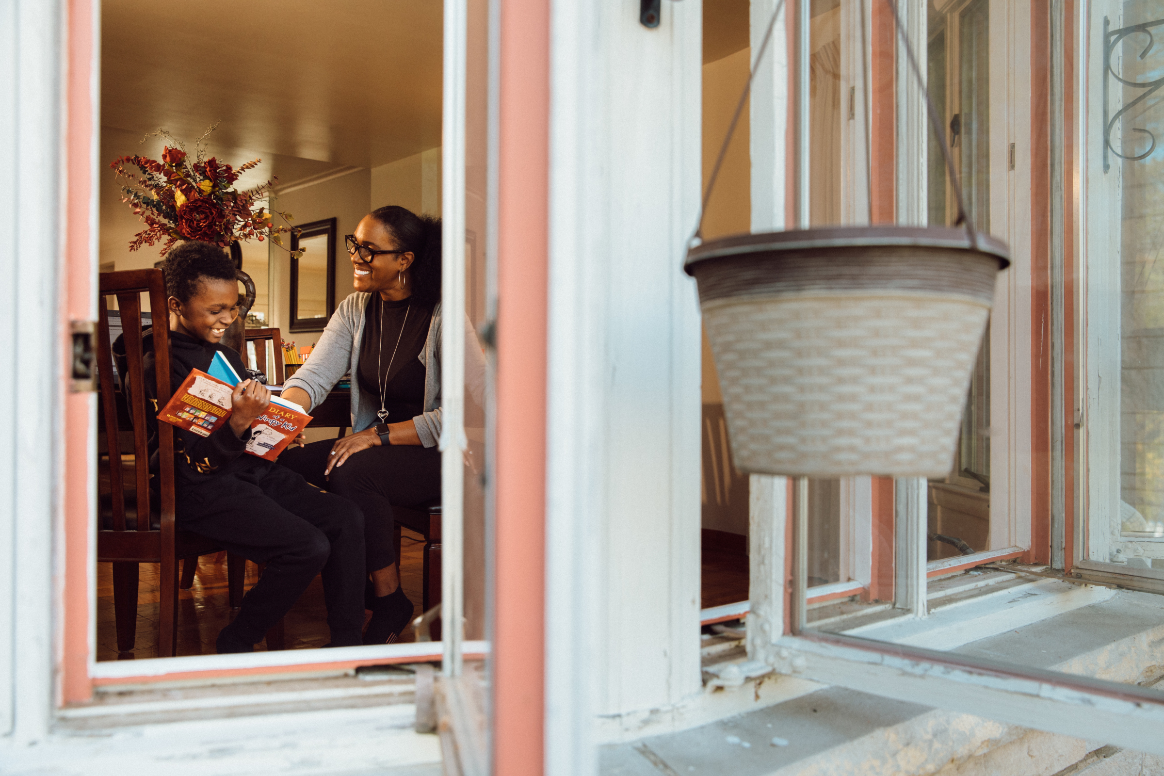 A view through the window of a mom and her student reading at home.