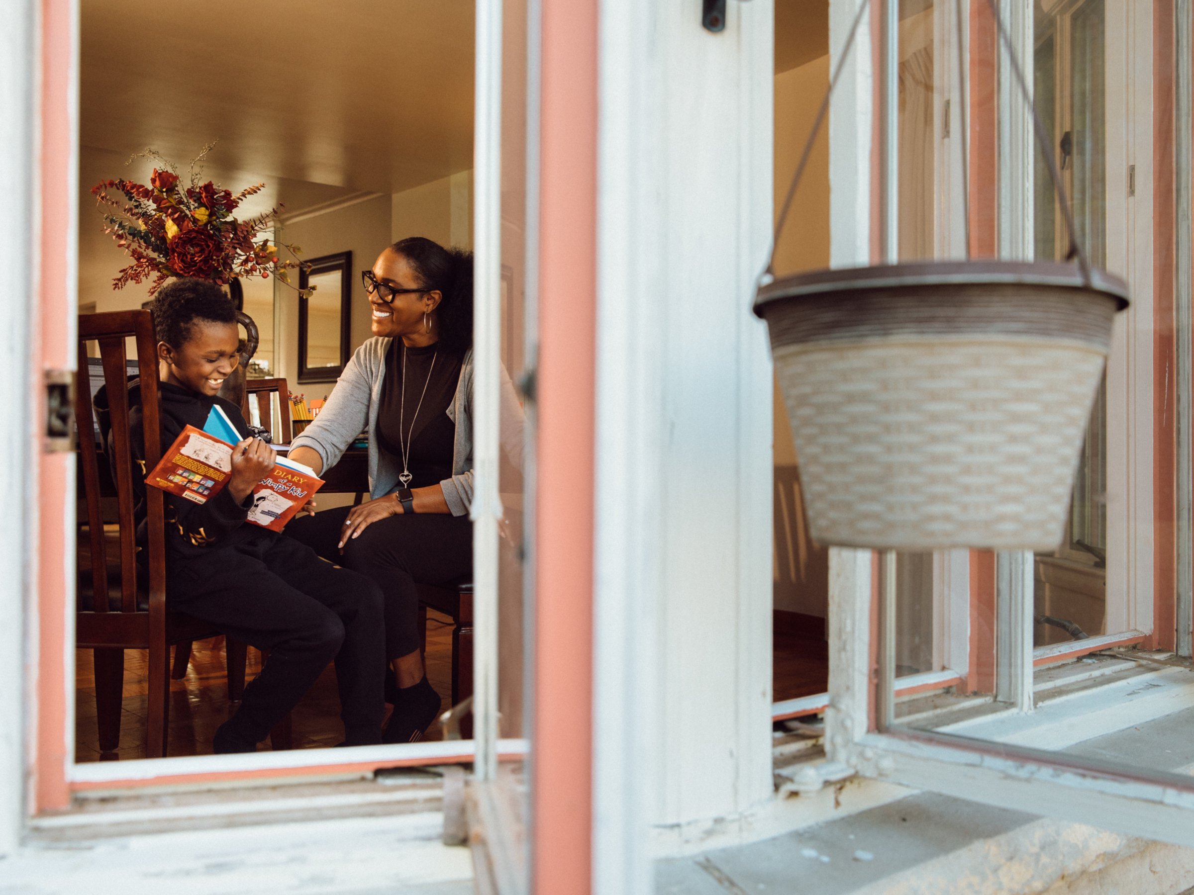 A view through the window of a mom and her student reading at home.