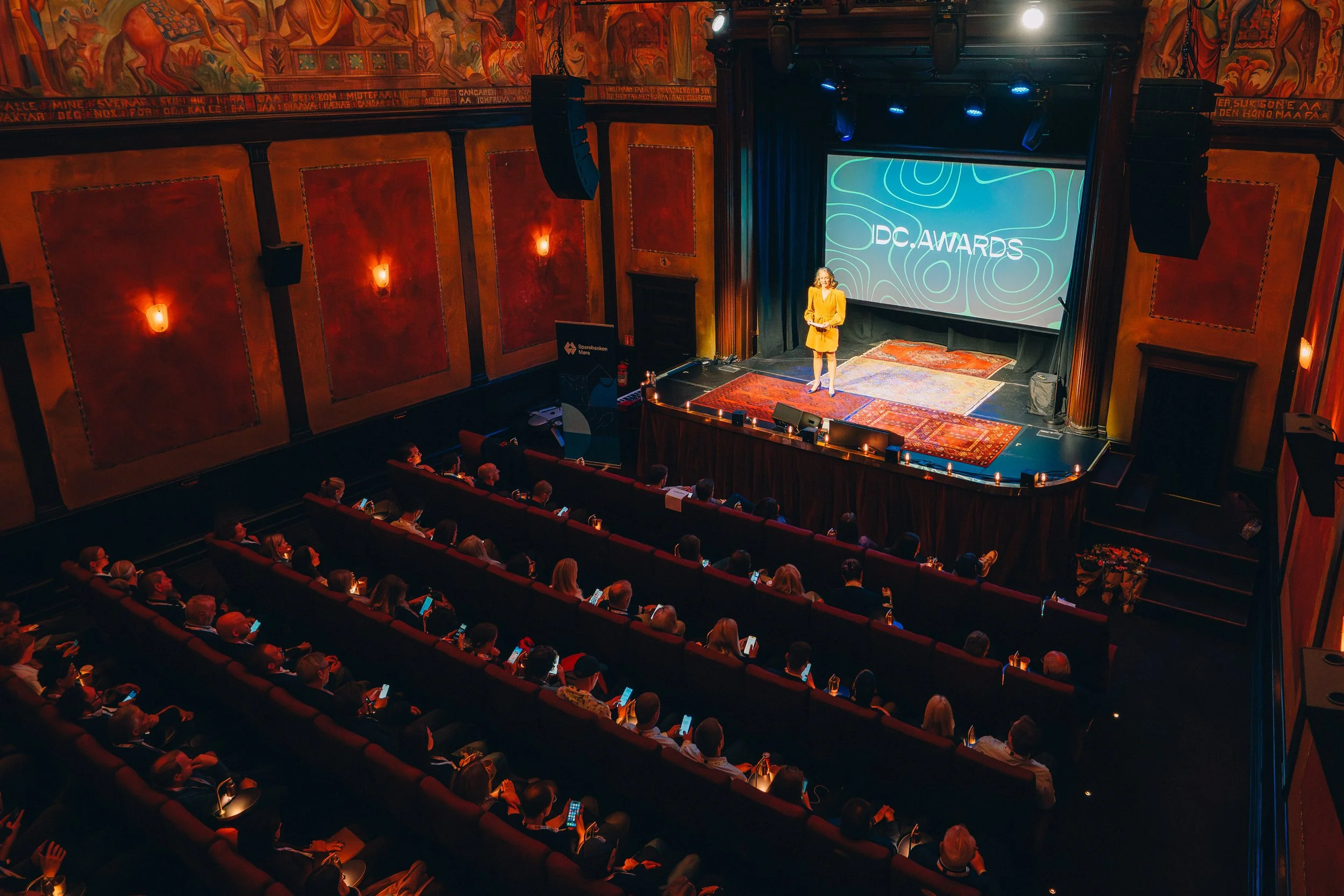 Foto av en kvinne på en scene med en stor skjerm bak seg der det står IDC Awards.