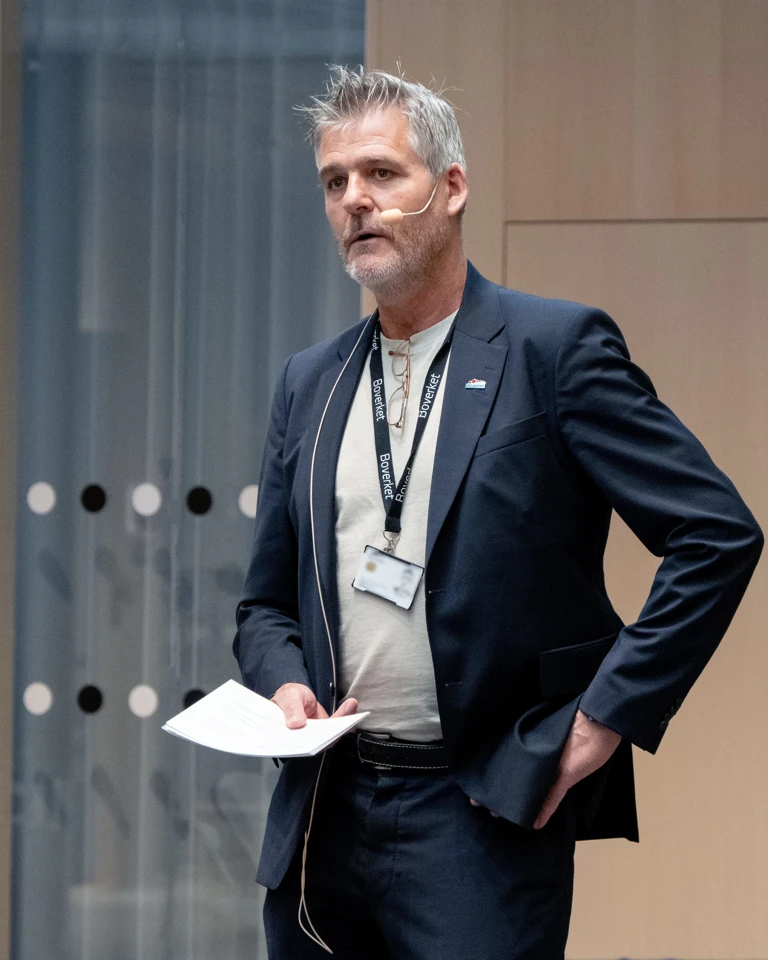 Foto av Lennart Andersson i mørk dress som står og holder et foredrag.
