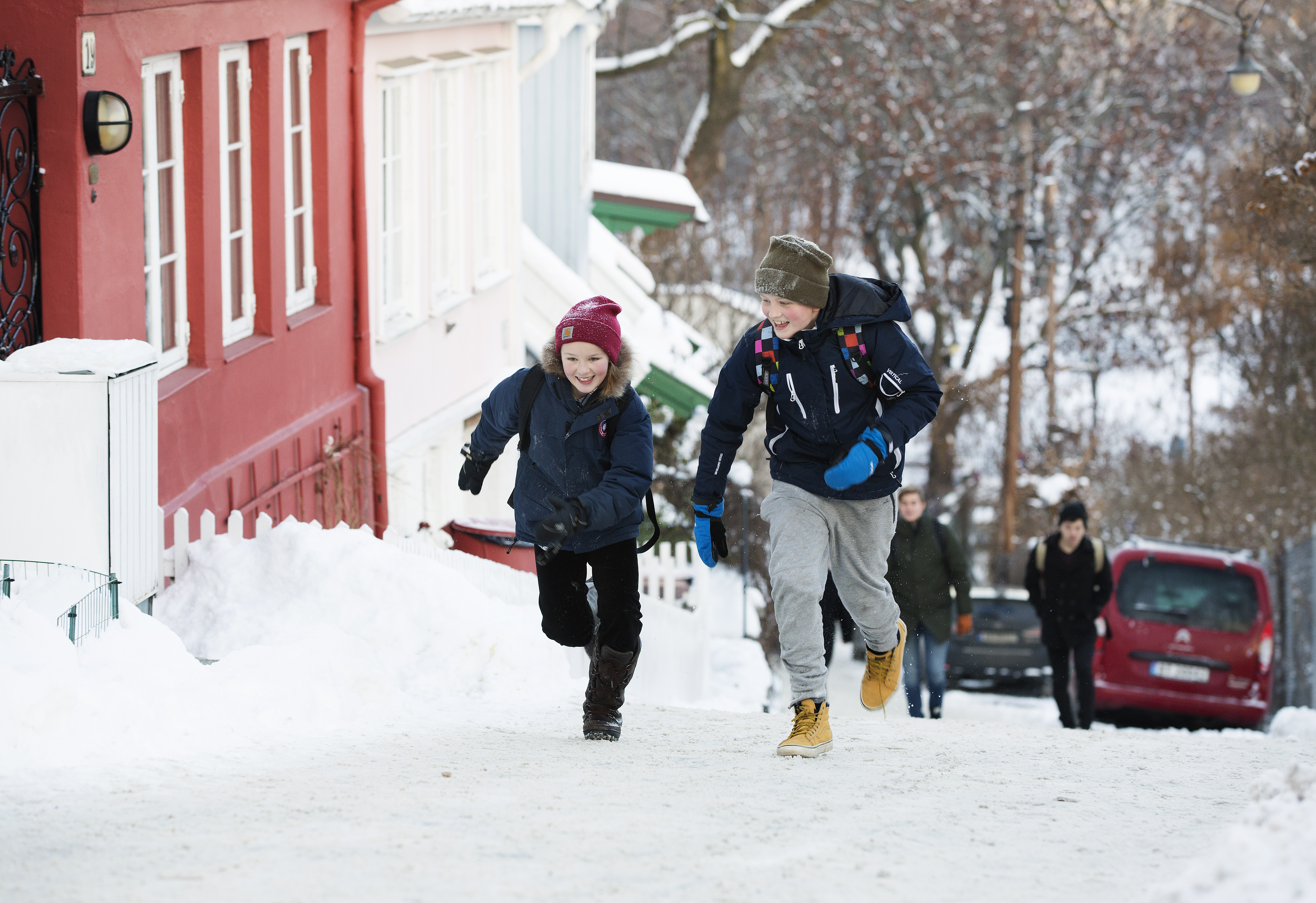 Foto av to barn som løper opp en snøkledd bakke i byen.