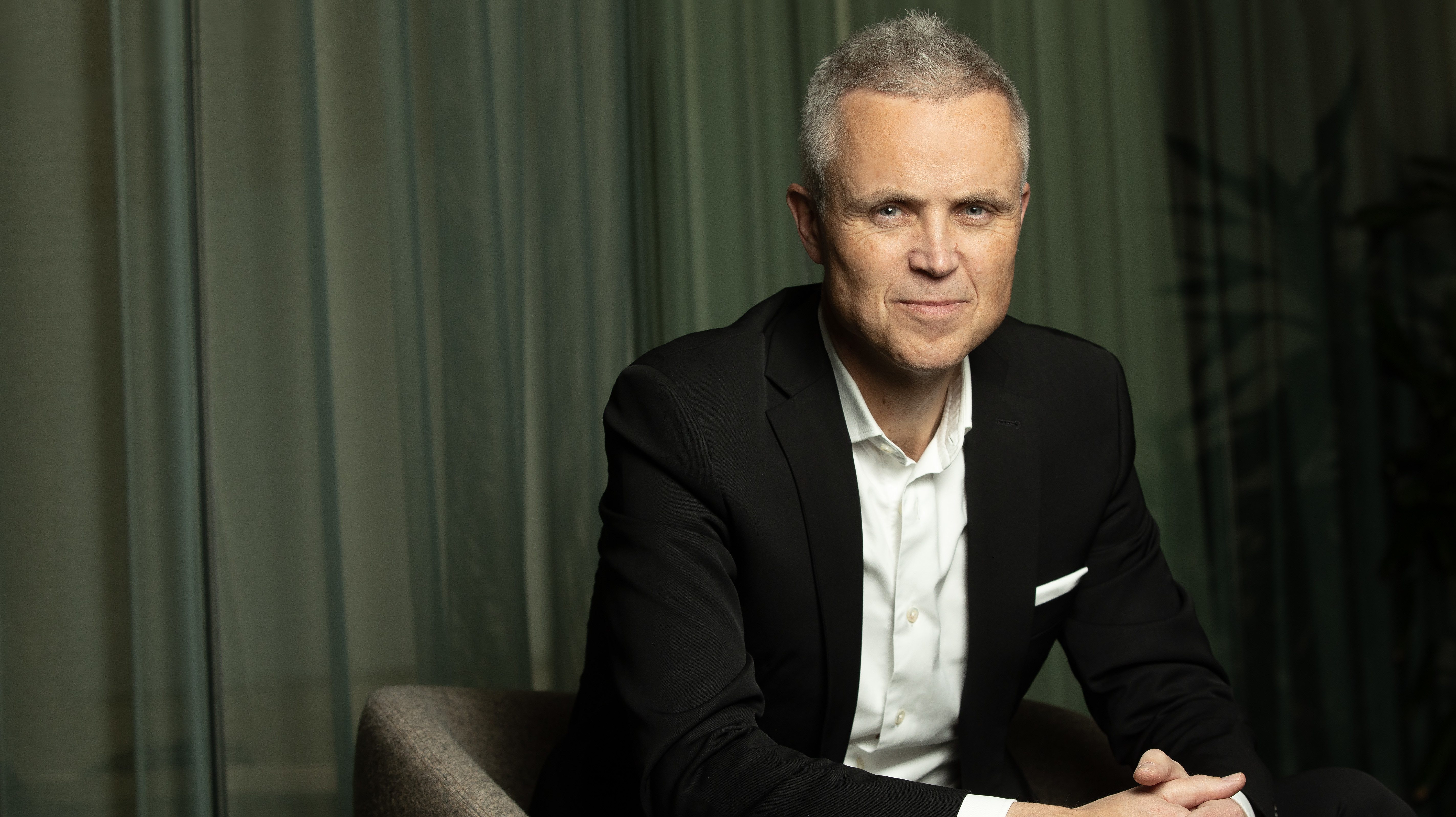 Foto av Tor Inge Hjemdal som sitter fremoverlent i en stol med svart dress og folede hender.