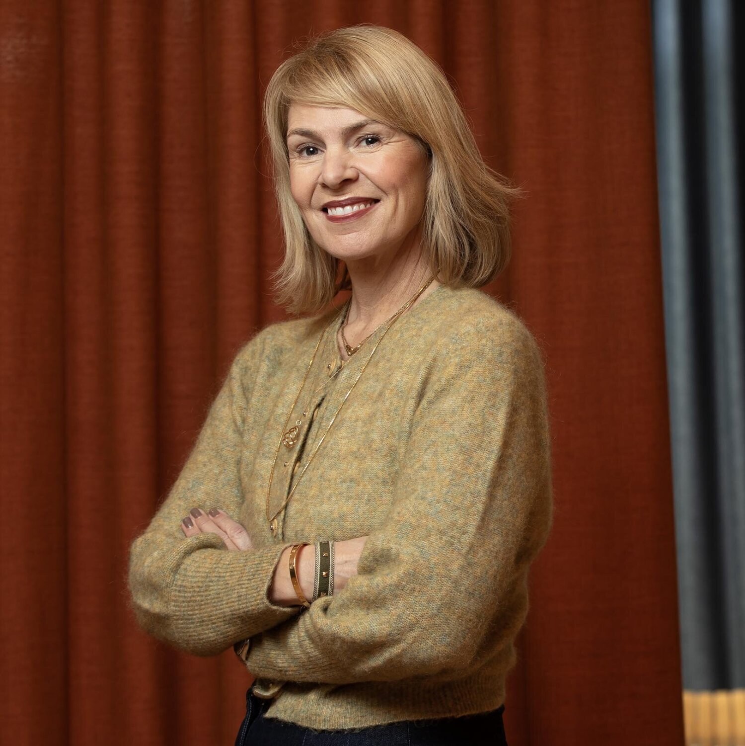 Foto av Anne smilende med blondt halvlagt hår og gulbeige jakke.