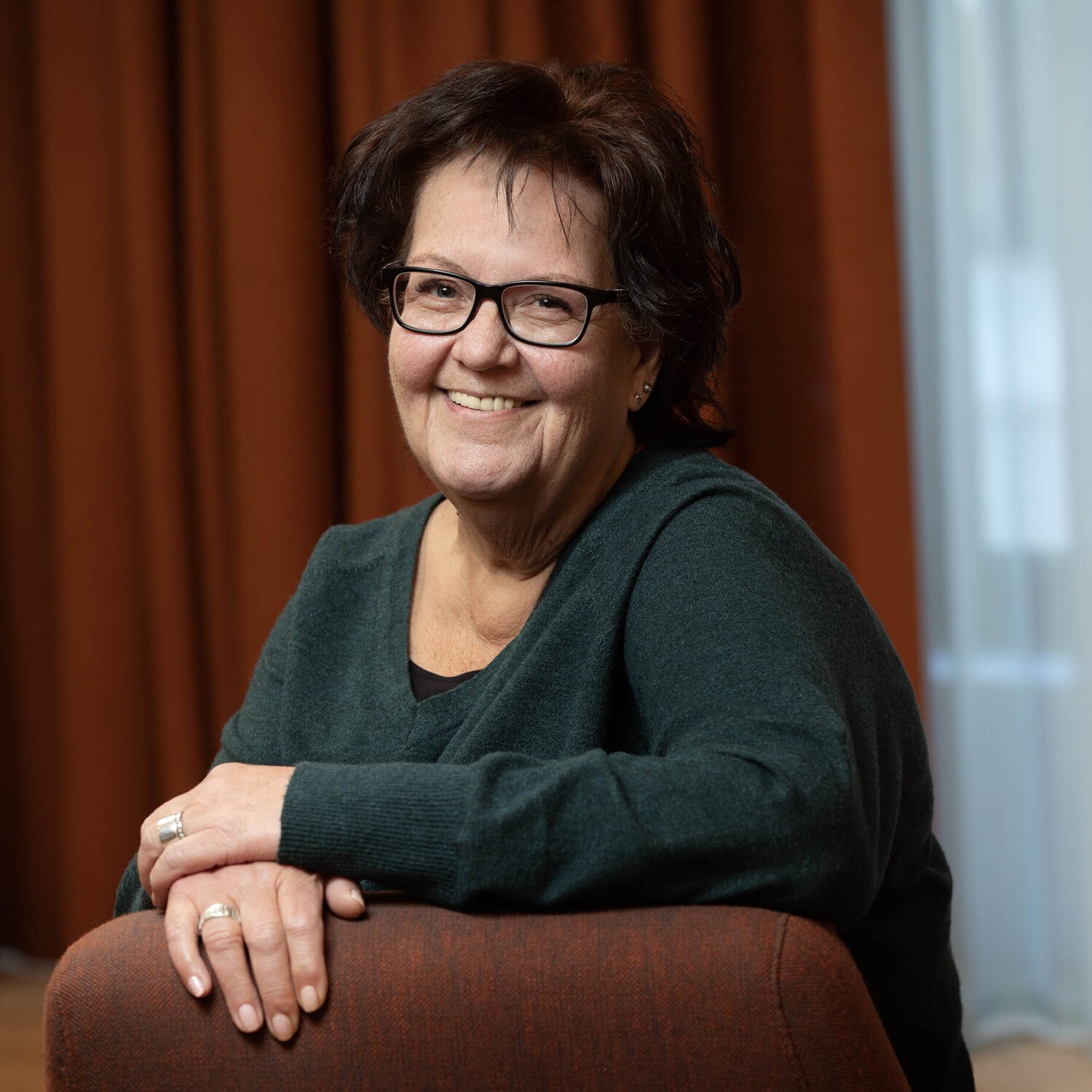 Foto av smilende Gro med kort, mørkt hår og briller med sort innfatning. Hun har på seg en mørkegrønn genser.