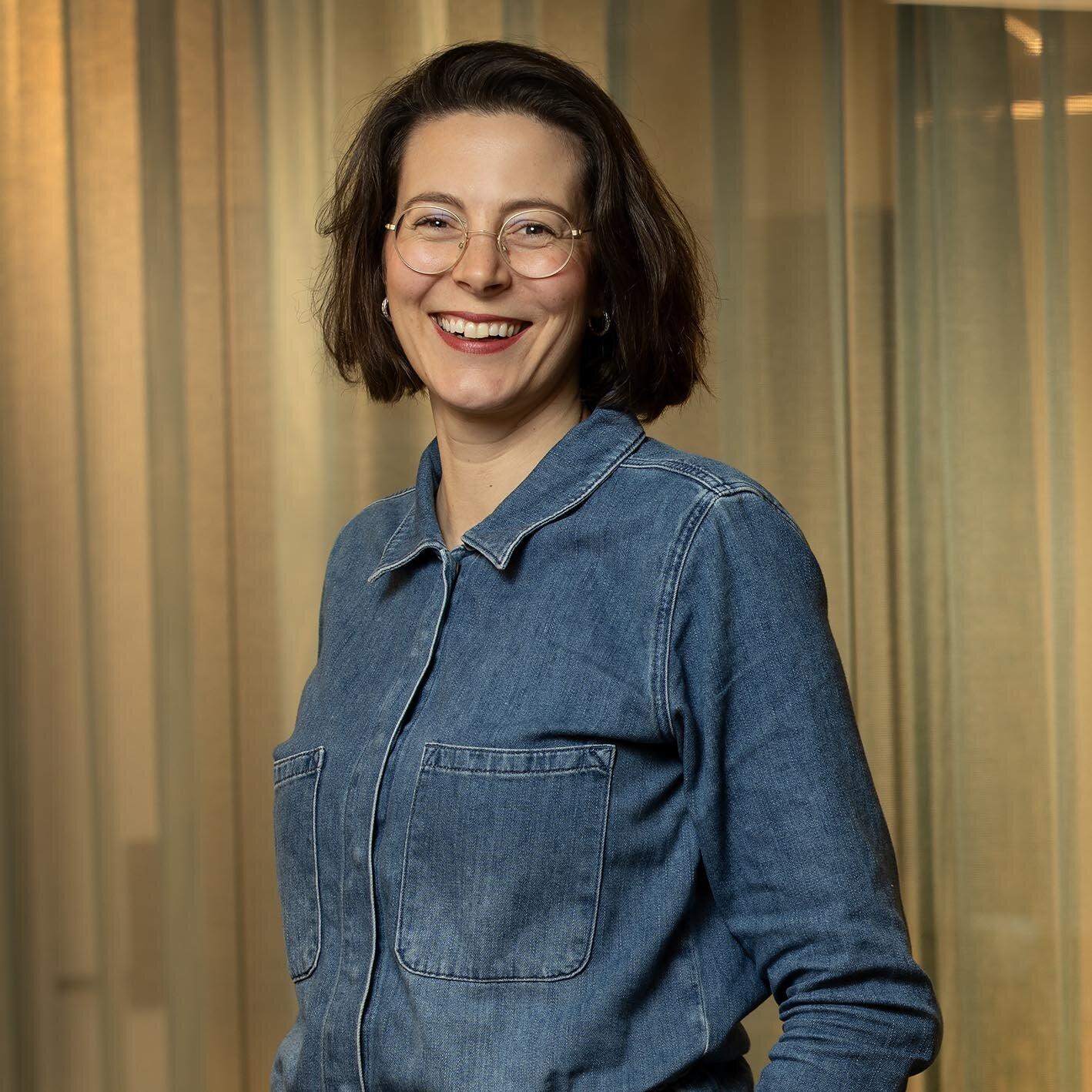 Foto av Kjersti med et varmt smil og kort, mørkt hår. Hun har biller med tynn, gylden innfatning og har på seg en jumpsuit i blå denim.