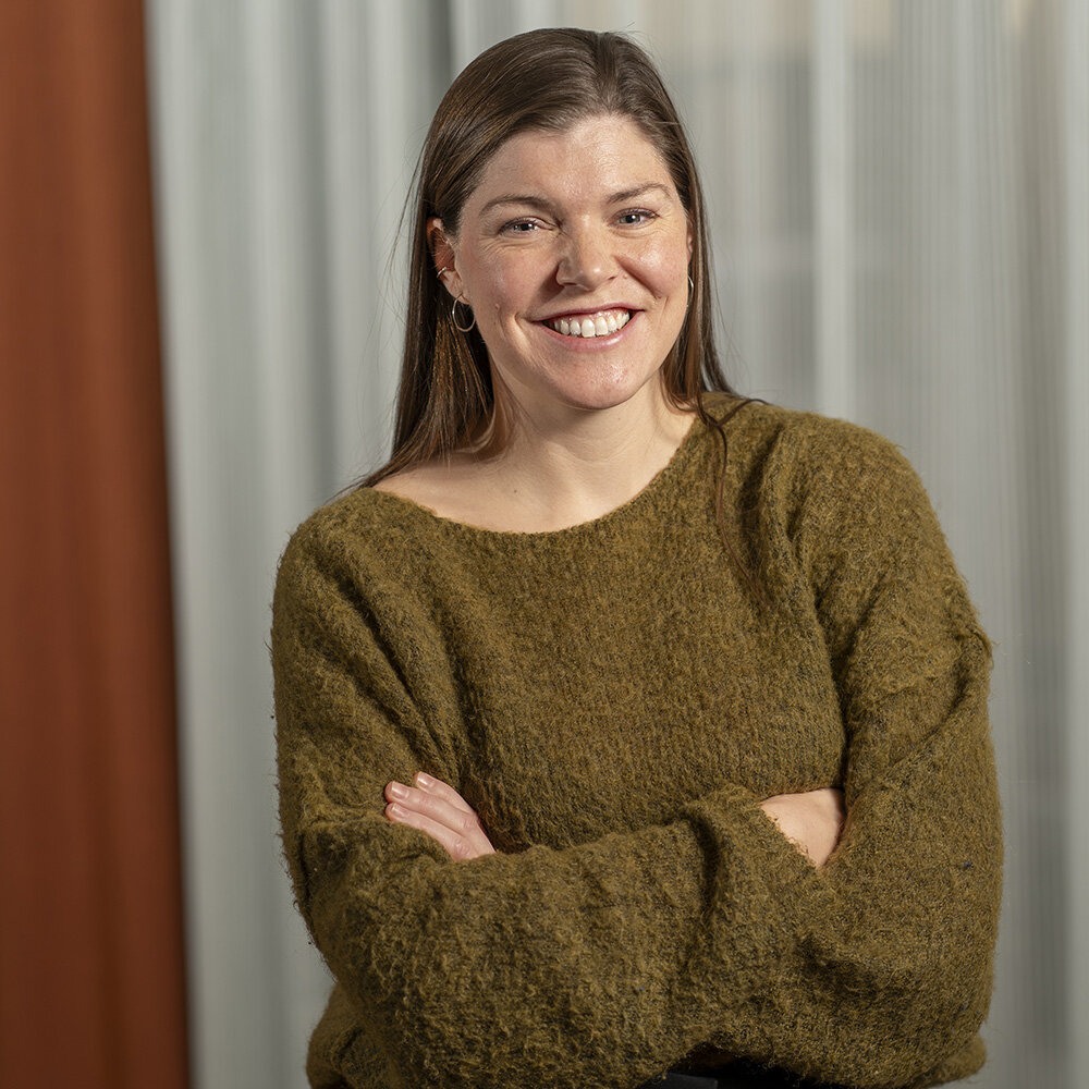 Foto av Kristin med mørkt utslått hår og ser smilende mot kamera.