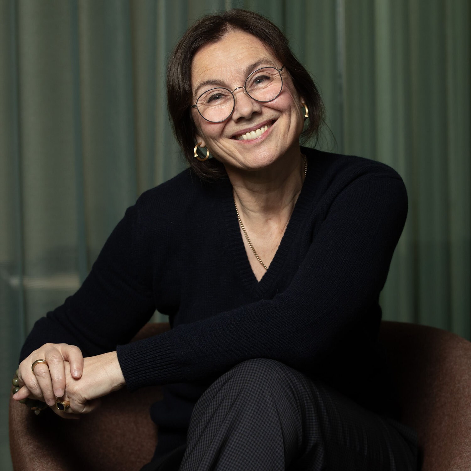 Foto av Tone smiler med oppsatt mørkt hår, briller, gullringer i ørene og sort v-genser.