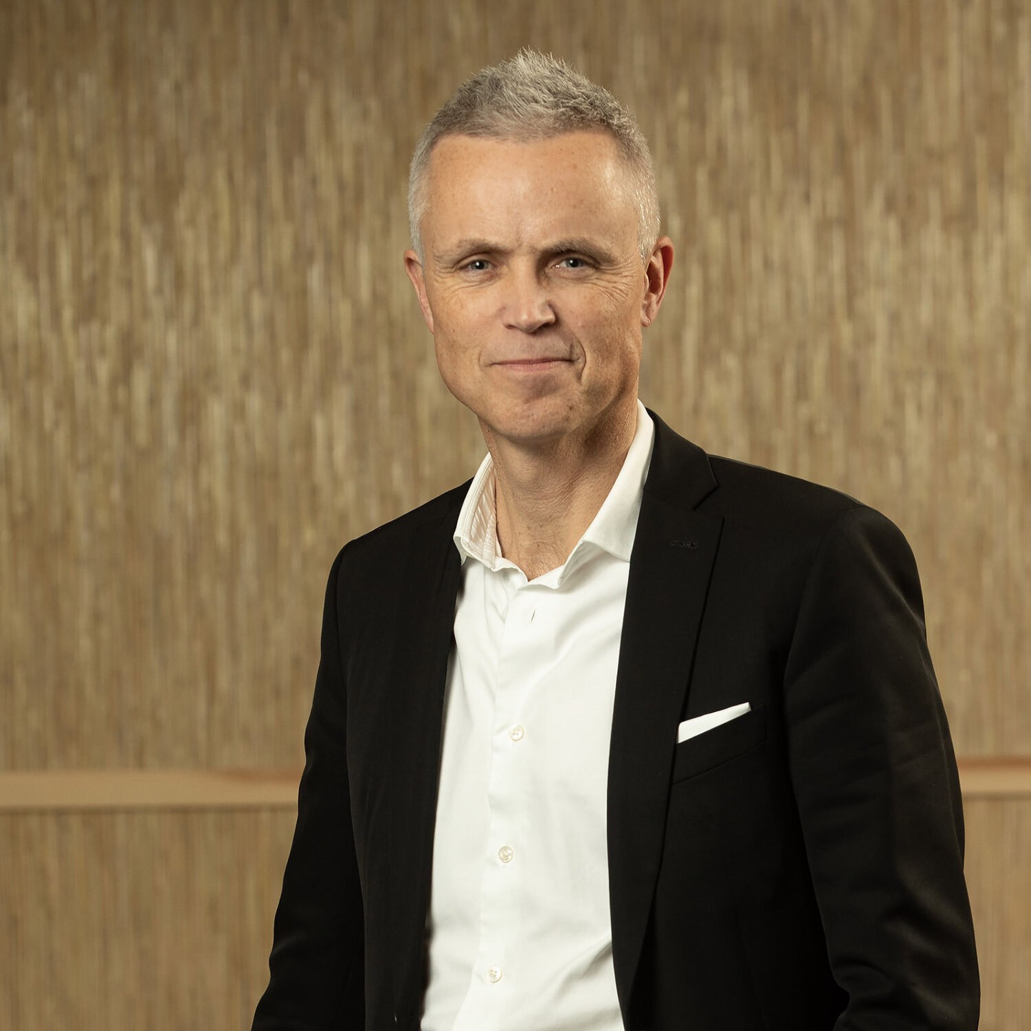 Foto av Tor Inge med et lite smil, kort, grått hår, sort dressjakke og hvit, åpen skjorte.