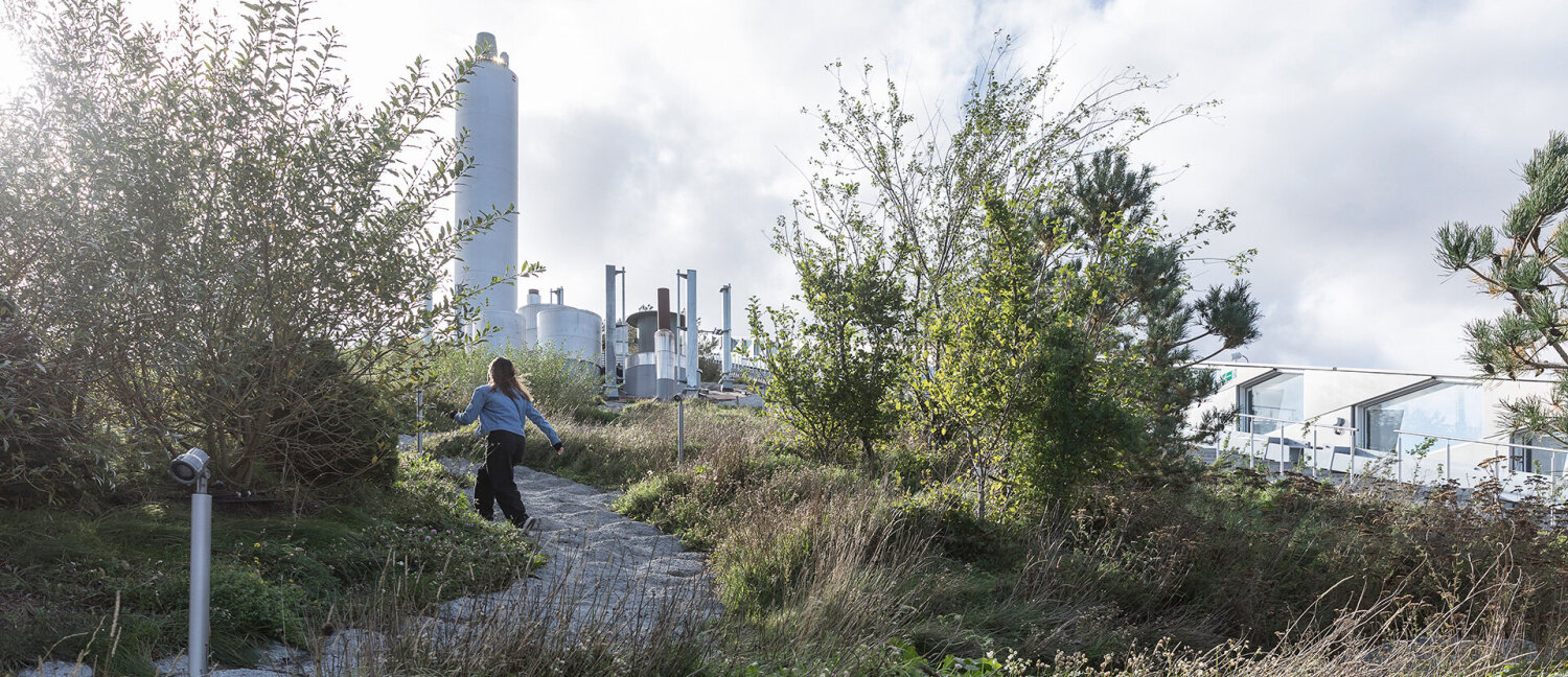 Foto av Copenhill i Danmark der et barn løper opp en naturskjønn bakke med industripiper i bakgrunnen.