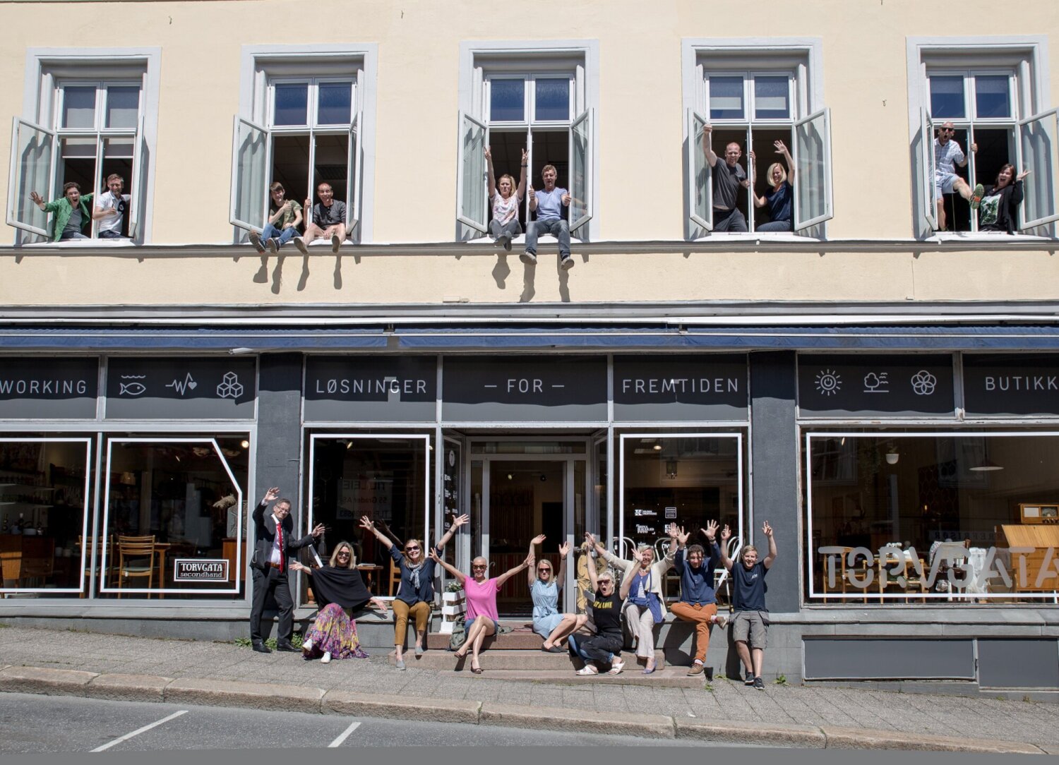 Foto av et lokale på bakkeplan med blide mennesker i både dører og vinduer.