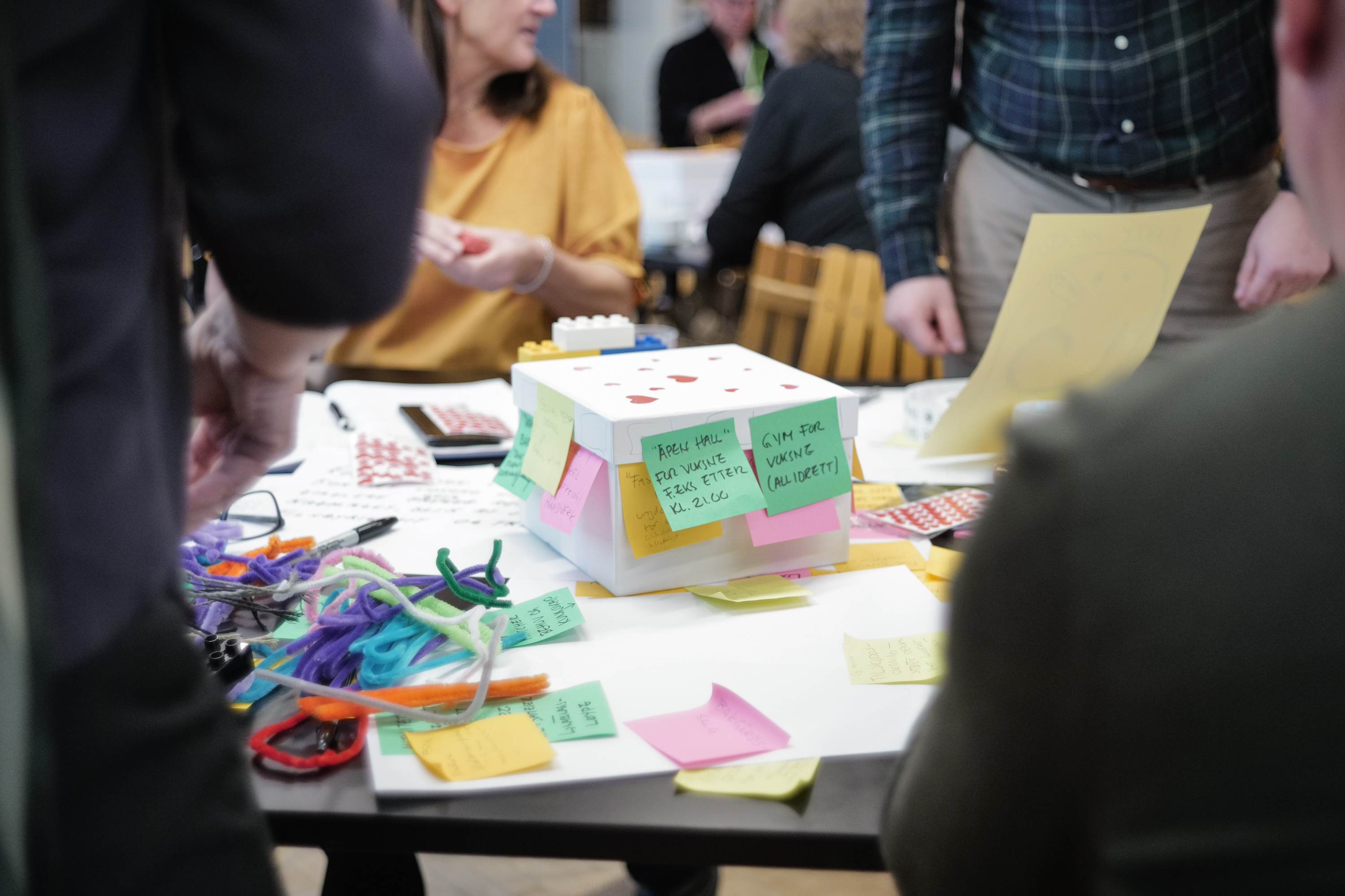 Foto av et bord med hender som bygger en liten prototype med papir, post-its og pipestilker.