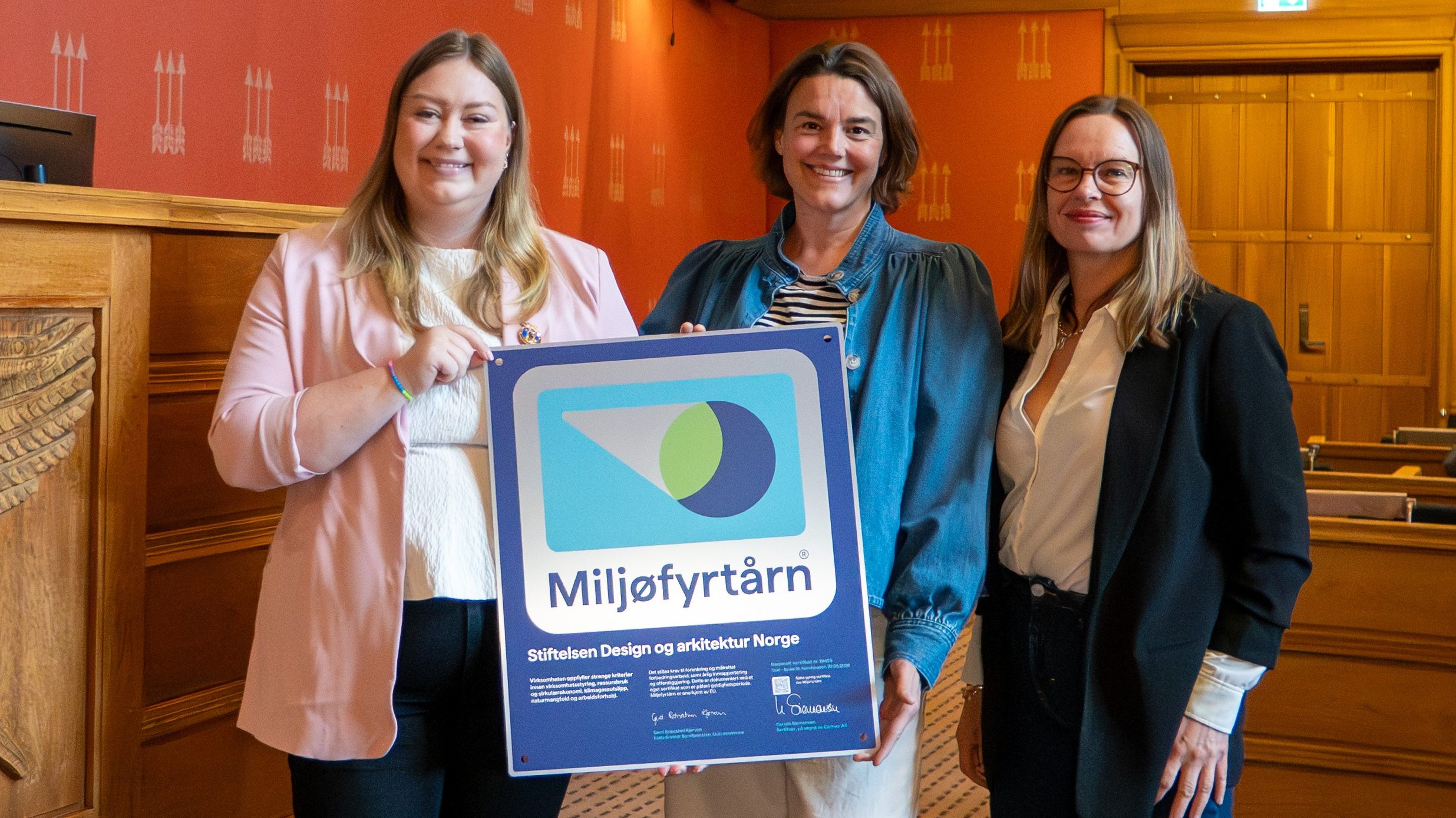 Tre smilende kvinner viser frem et stort skilt med en illustrasjon i blått og grønt med Miljøyrtårn skrevet nederst med stor skrift.