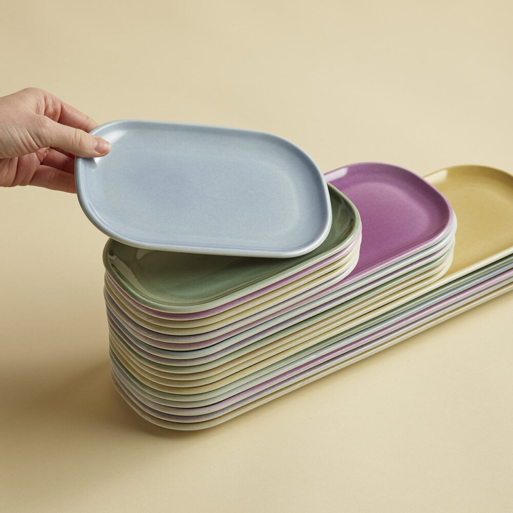 Nærbilde av en hånd som løfter en tallerken fra en stabel med fargerike tallerkener.