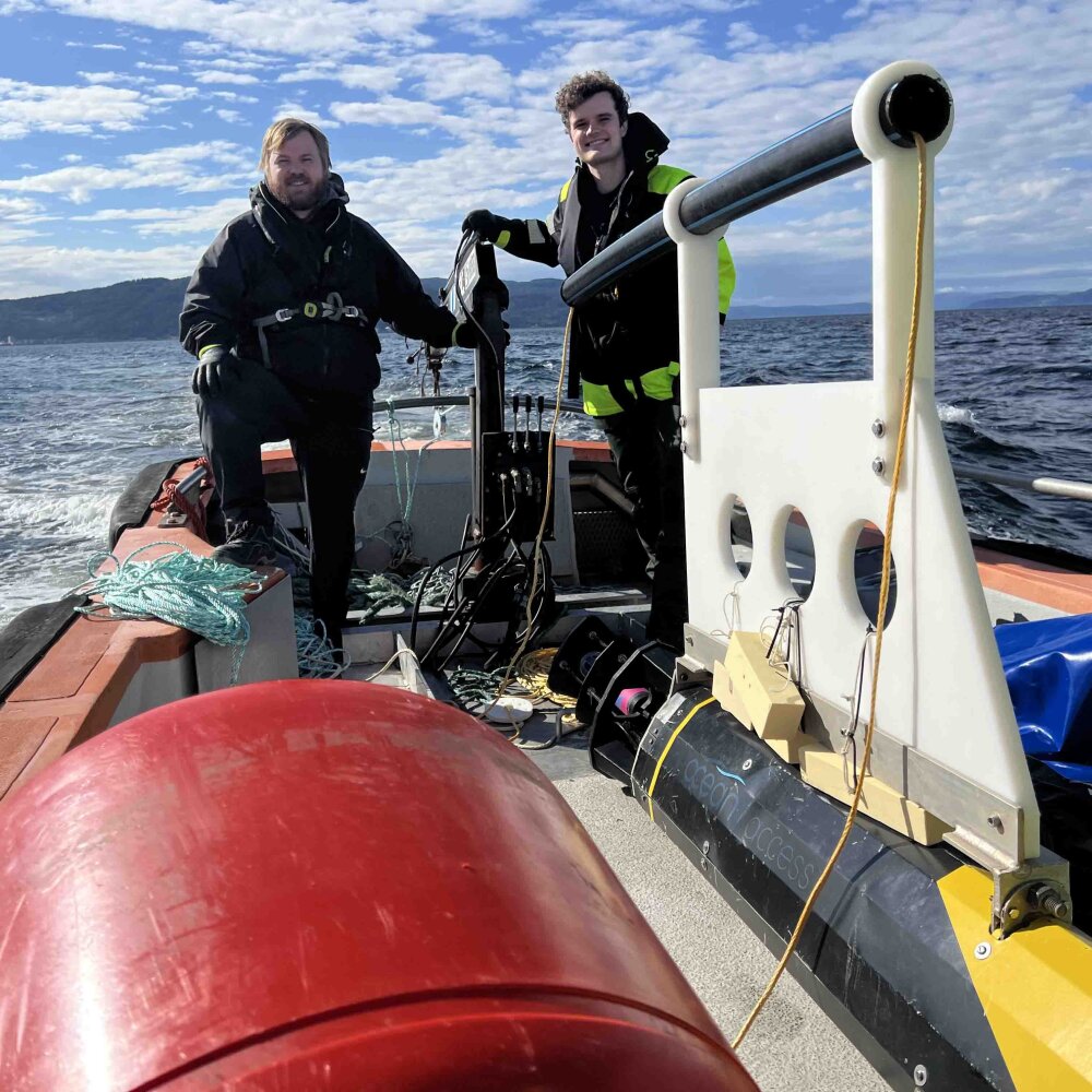 Foto av to menn som står på en båt ute på sjøen.