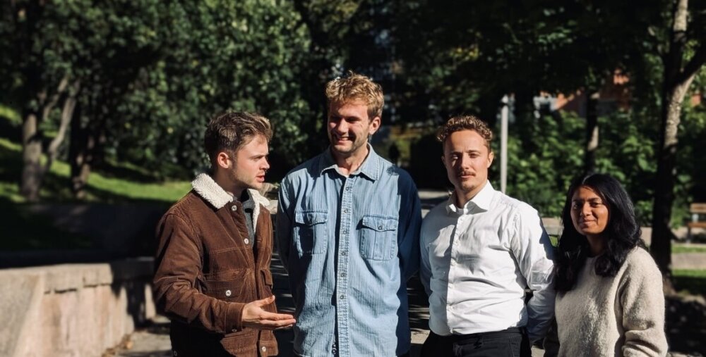 Foto av fire unge, smilende mennesker som står med armene rundt hverandre vendt mot kamera.