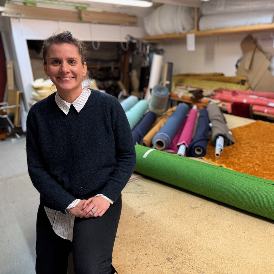 Foto av prosjektleder Siri Sanden som står smilende foran et bord med stoffruller.