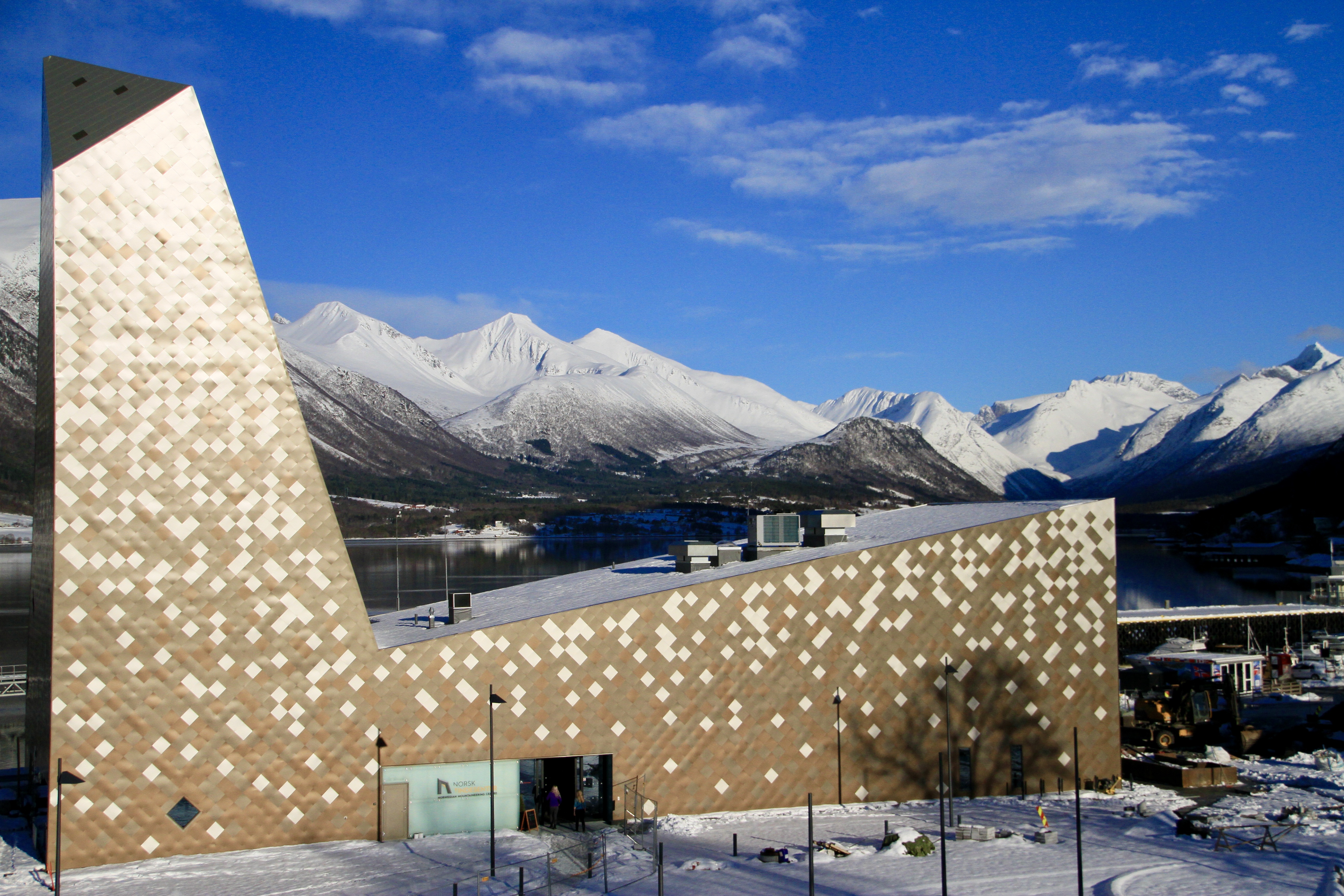 Foto av Norsk Tindesenters fasade som er formet som et fjell. I bakgrunnen, snødekte fjell.