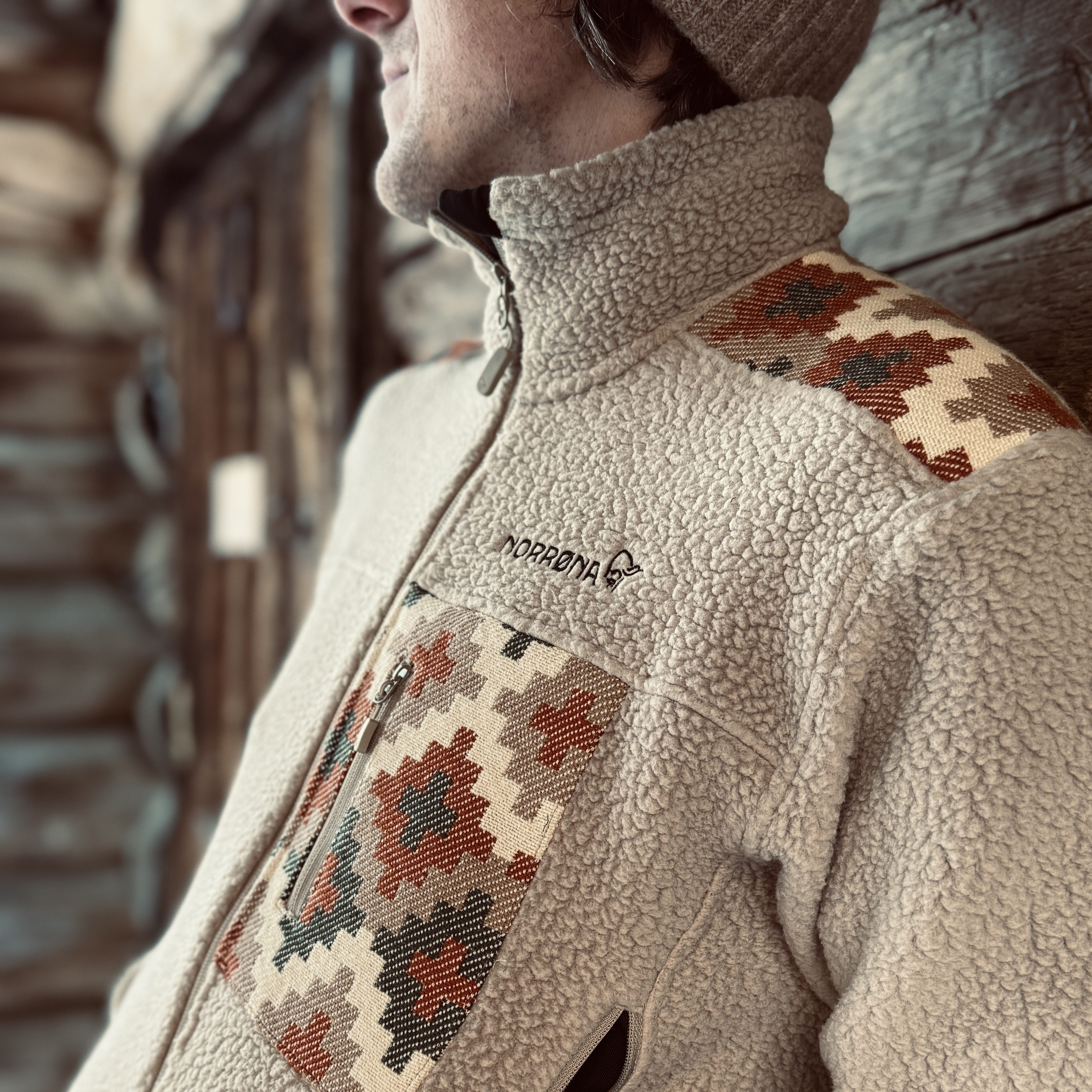 Nærbilde av en beige fleecejakke med elementer av tradisjonelle norske mønstre og logoen til Norrøna.