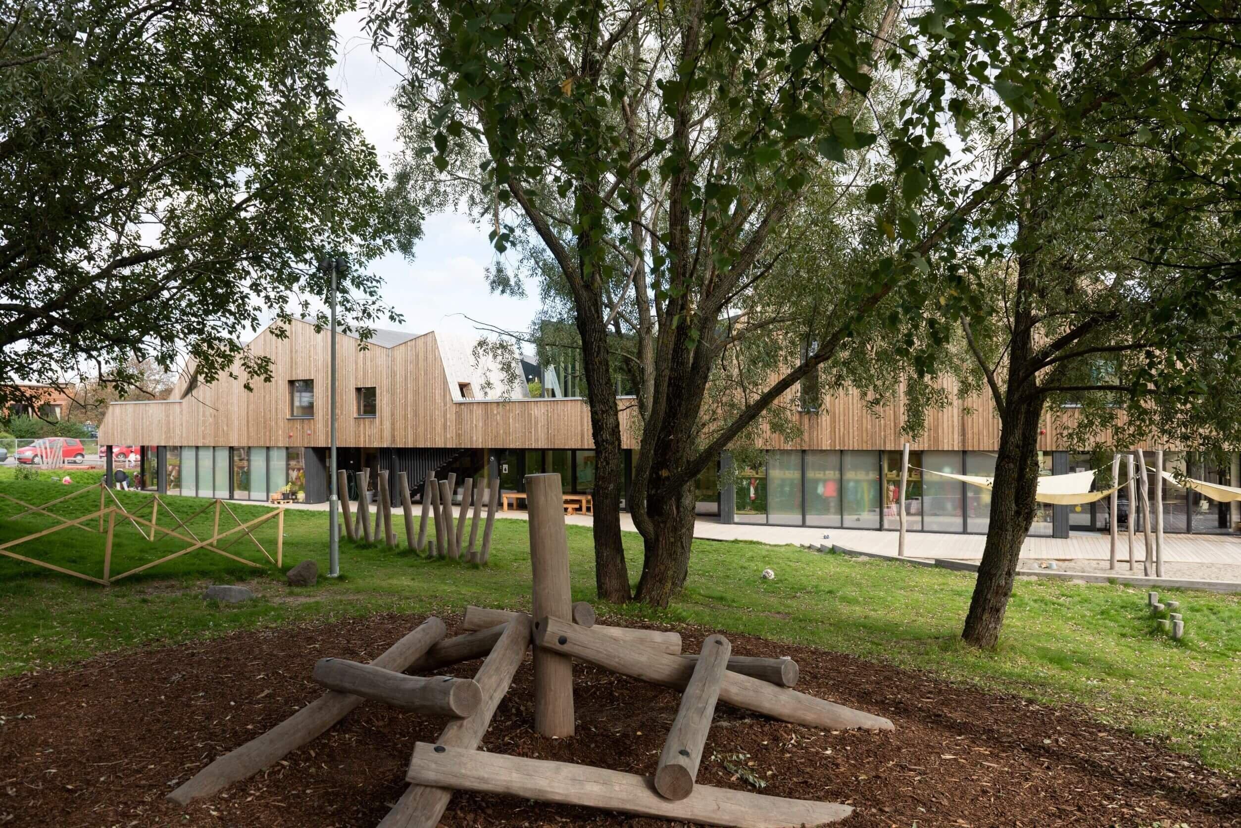 Uteområde med lekeplass av trestammer og trær bak.