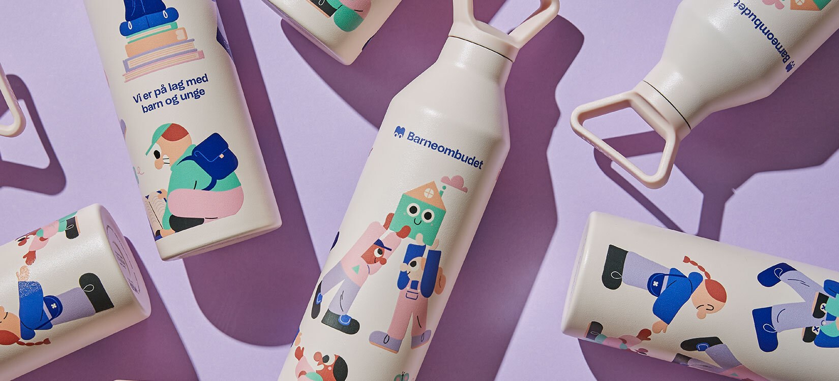 Bildet viser flere drikkeflasker som ligger på en rosa bordplate. Flaskene har fargerike illustrasjoner av vennlige figurer.