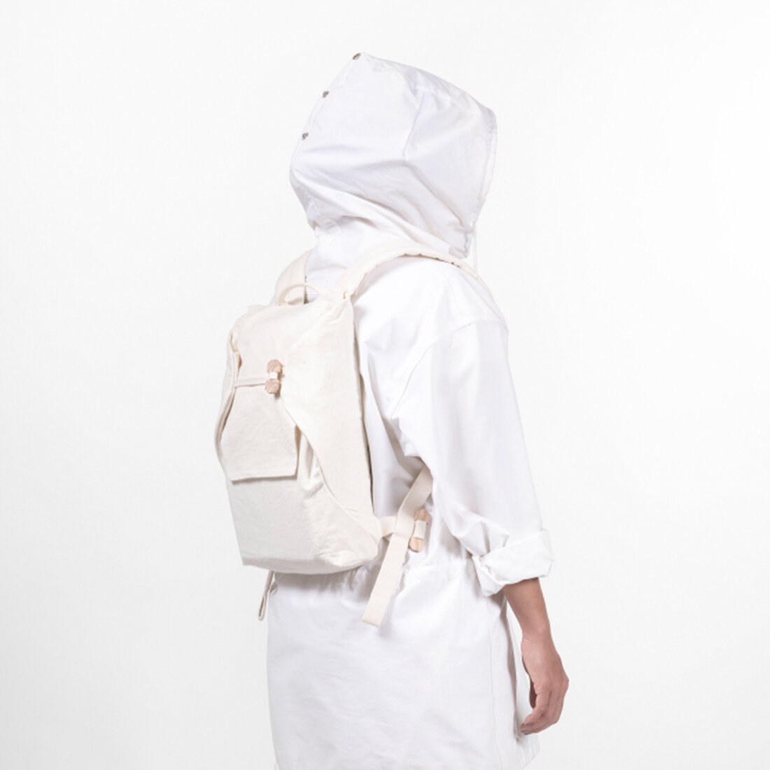 Studioportrett av en persons rygg. Personen er kledd i hvitt, med hvit hette, og har på sen en hvit ryggsekk.