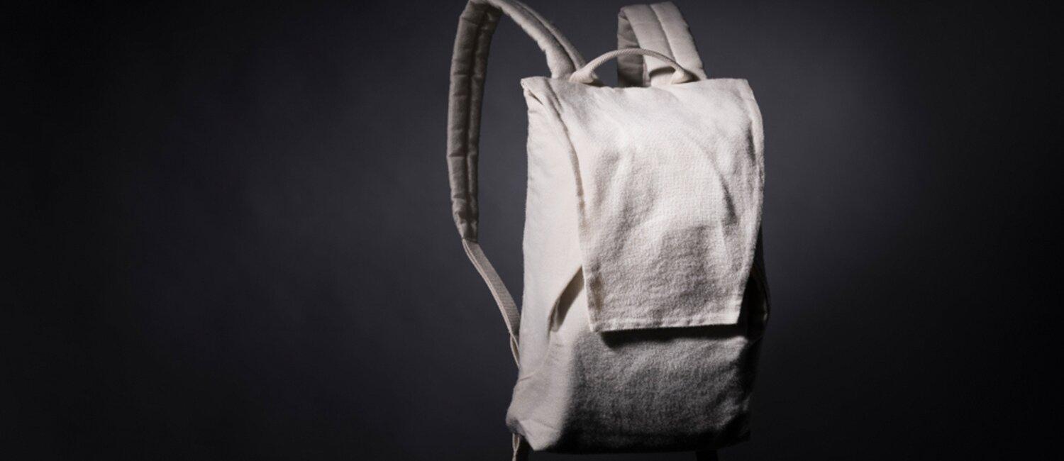 Produktfoto av en hvit ryggsekk. Enkelt, design uten mye detaljering. Den er utformet i et tekstil med en matt, til ru overflate – som minne om grov lin i uttrykket.