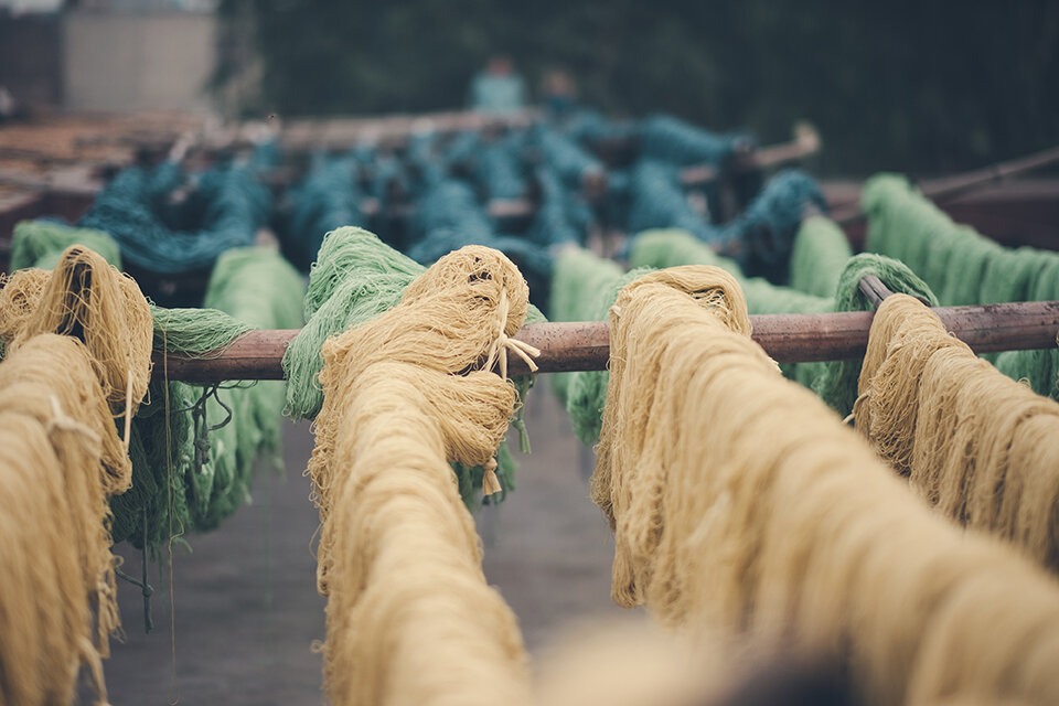 Fargede tråder i sennepsgul, grønn og sjøgrønn henger til tørk på trestammer.