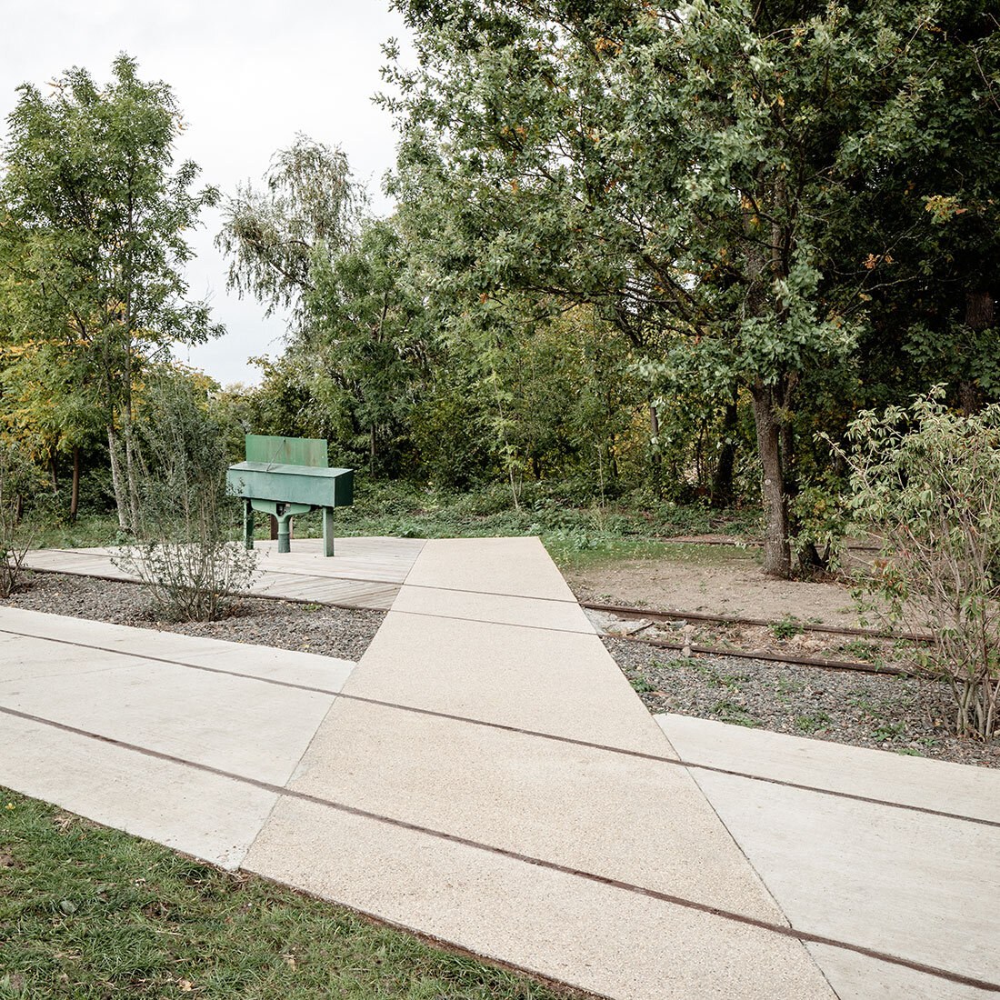 To parallelle jernbanespor ses i bakken. Ett av sporene er muret opp slik at overflaten er jevn. Rund ses skog og gress.