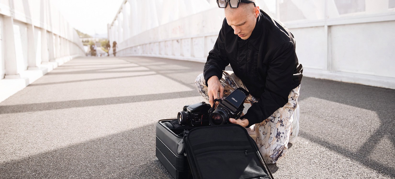 En mann sitter på huk og løfter et kamera ut av en åpen koffert.