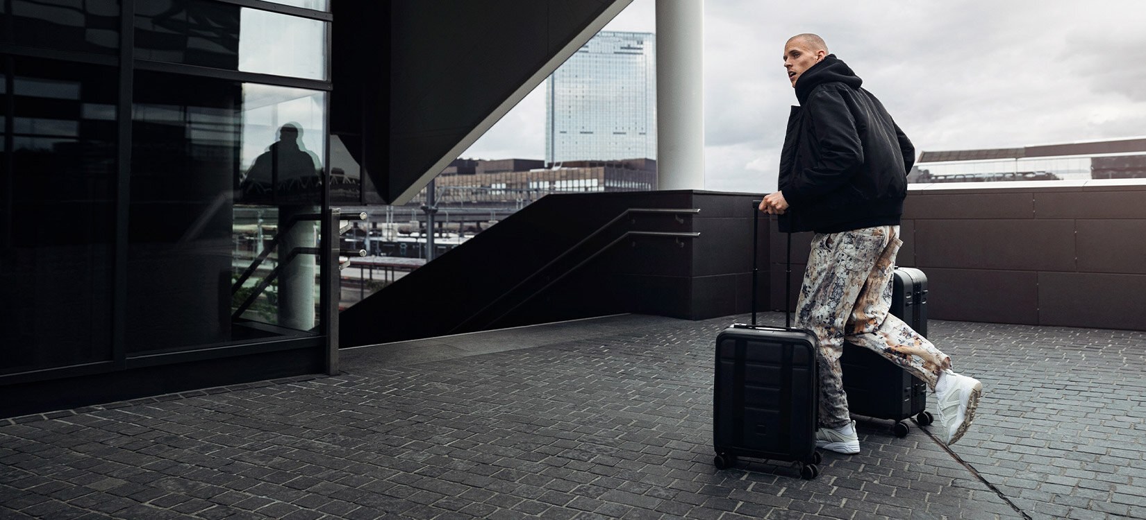 En mann med to trillekofferter går mot et trappeløp.