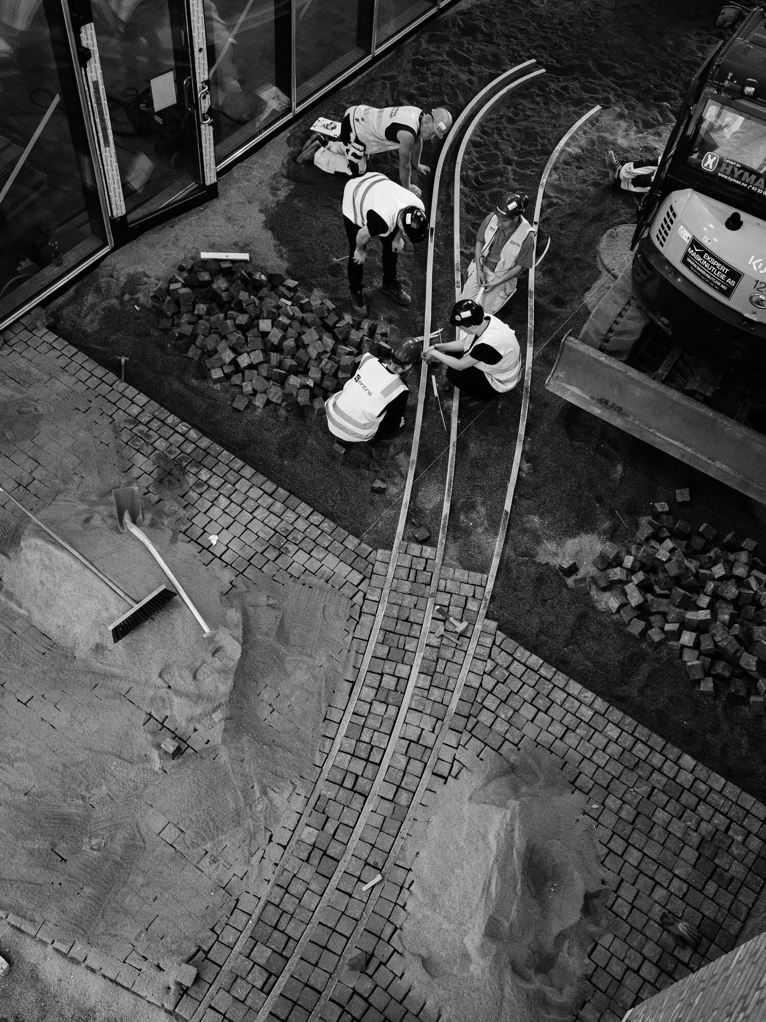 Anleggsarbeidere sitter og monterer lyskildene på bakken.