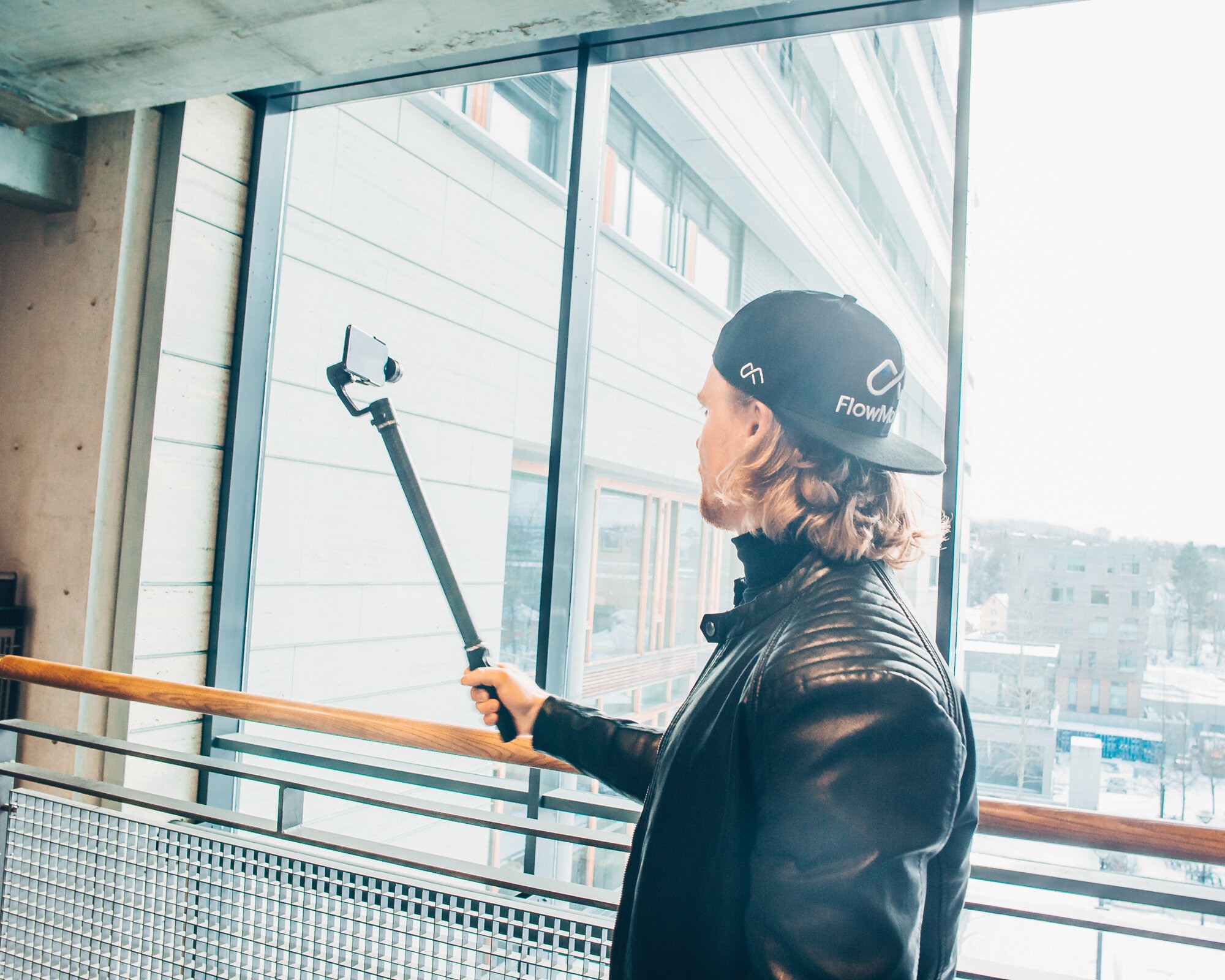 Bildet viser en ung mann bak fra som holder i et langt håndtak med en smarttelefon festet i enden.