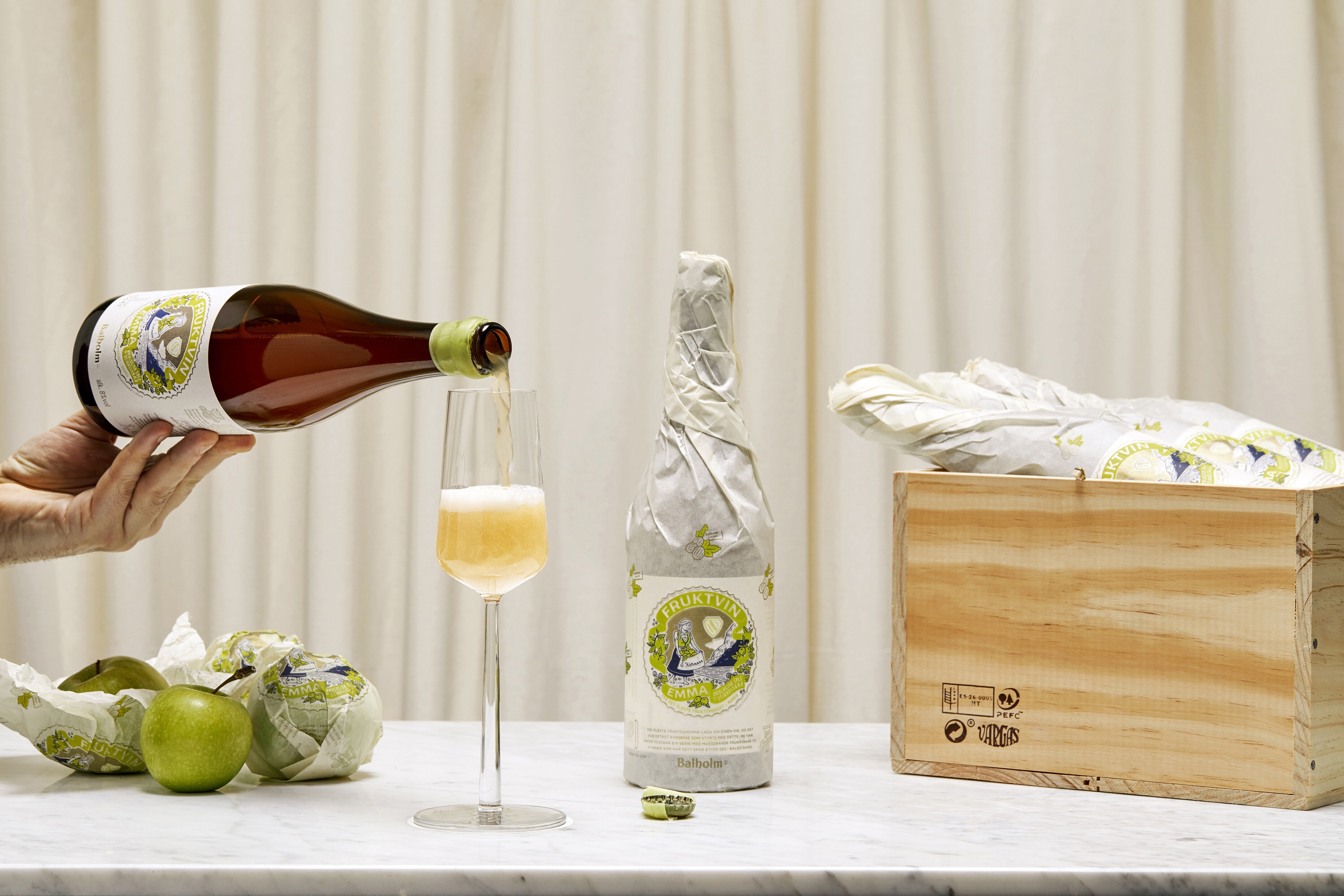 Foto av et stilleben der en hånd strekker seg inn og heller fruktvin i et vinglass.