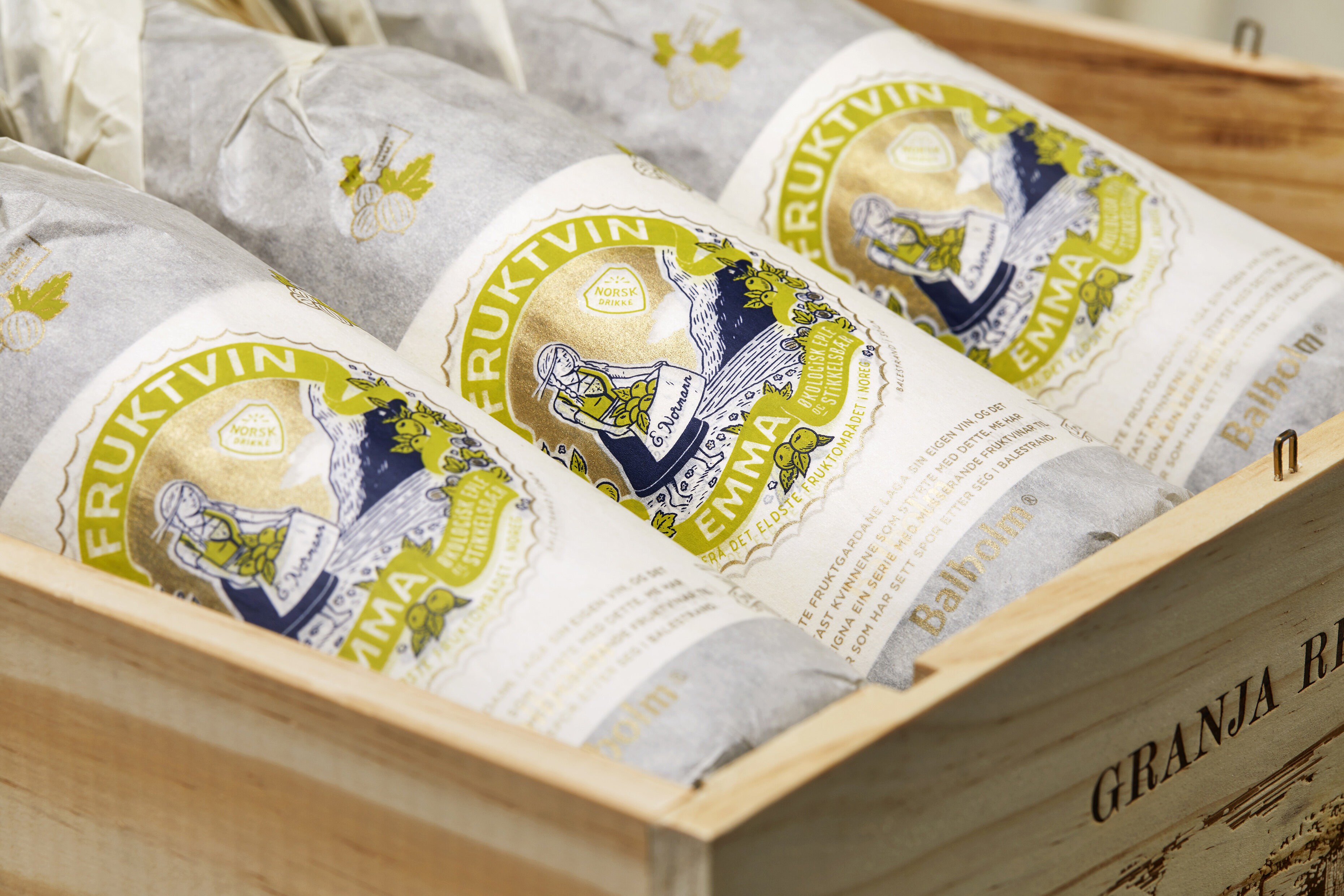 Tre flasker, innpakket i dekorert silkepapir, ligger i en trekasse.