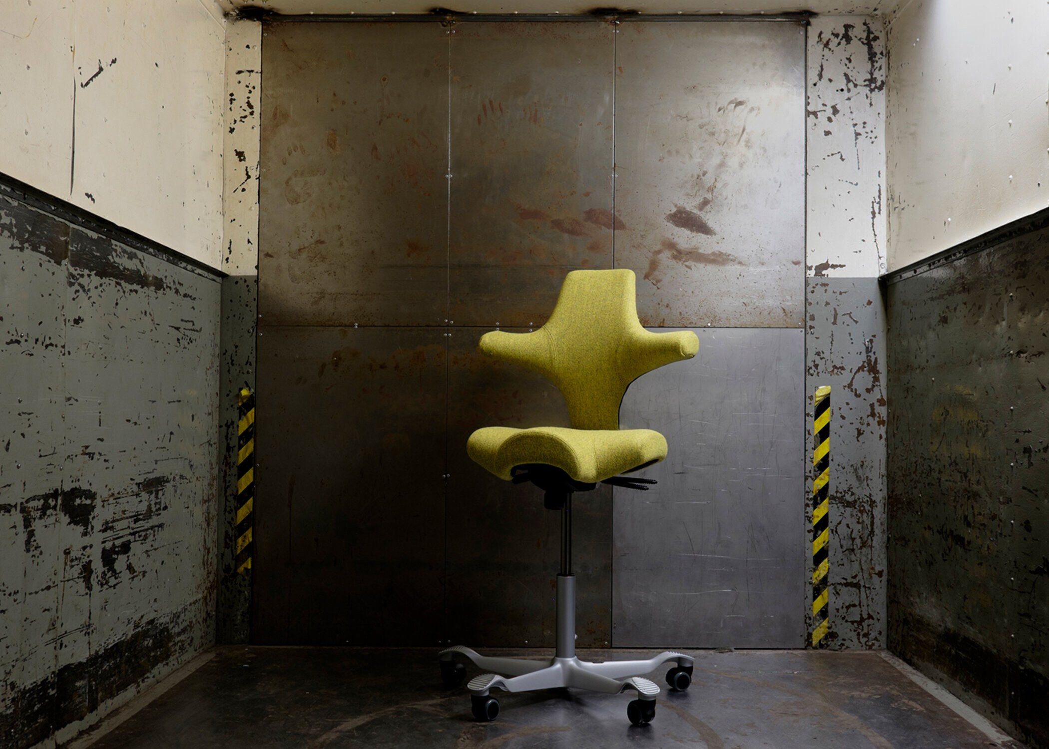 Et produktfoto av en kontorstol trukket i sennepsgult ullstoff – i industrielle omgivelser.