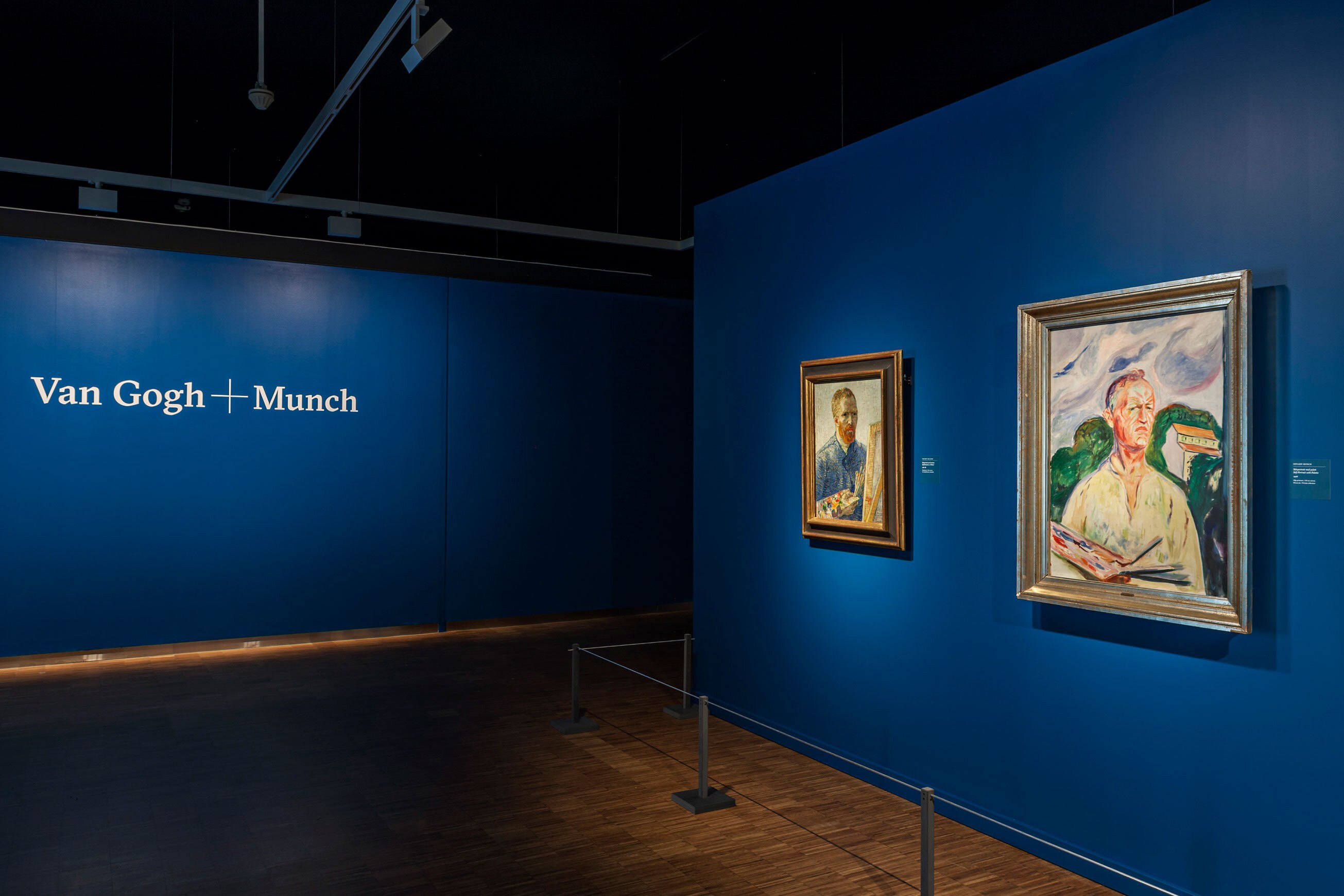 Utstillingssal med vegger malt i dyp blå. Tekst på veggen leser Van Gogh+Munch. Til høyre i bildet henger det to portrettmalerier.