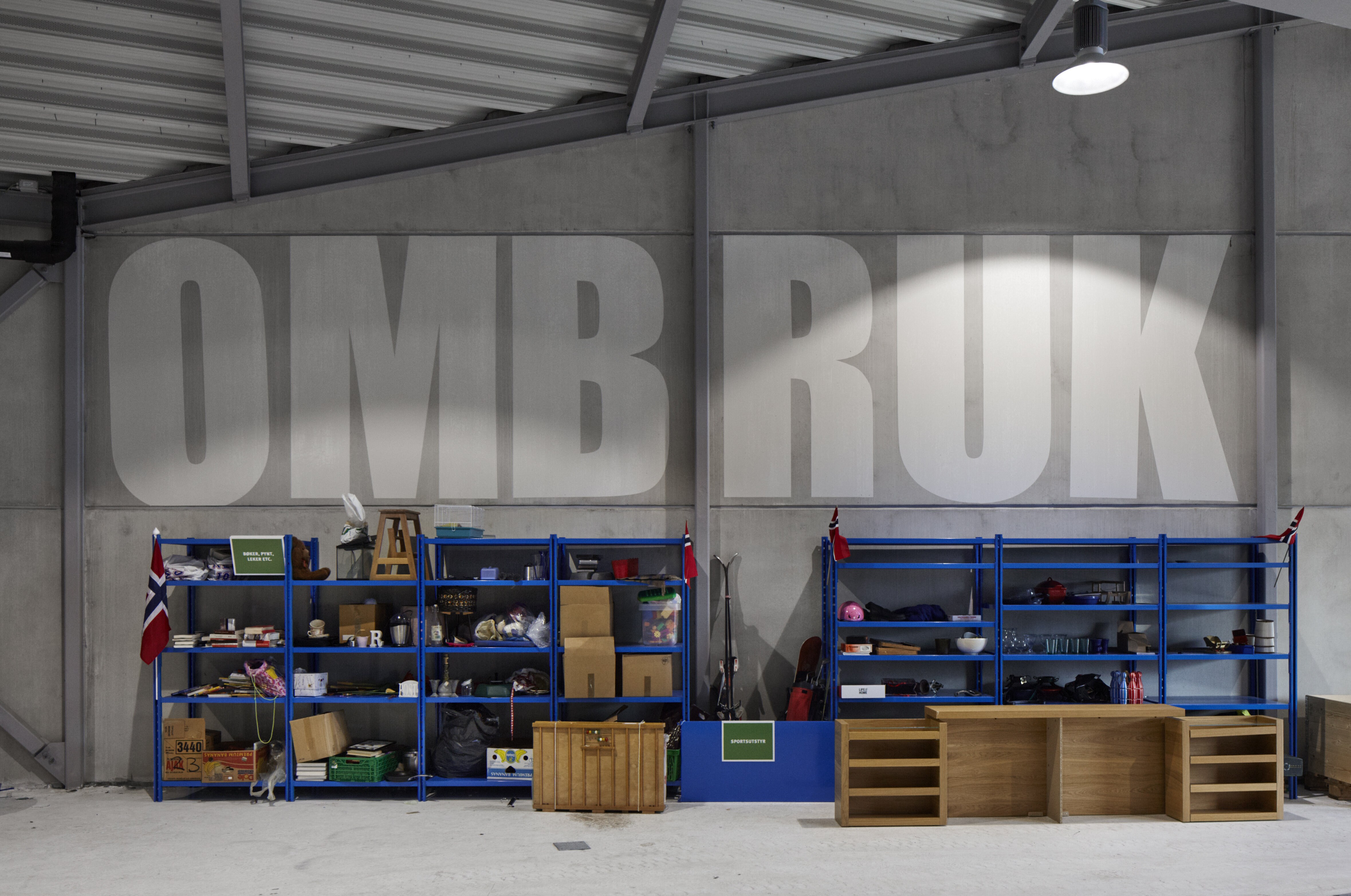 Interiørfoto av to blå reoler mot en betongvegg hvor det er skerevet "OMBRUK" med store bokstaver.