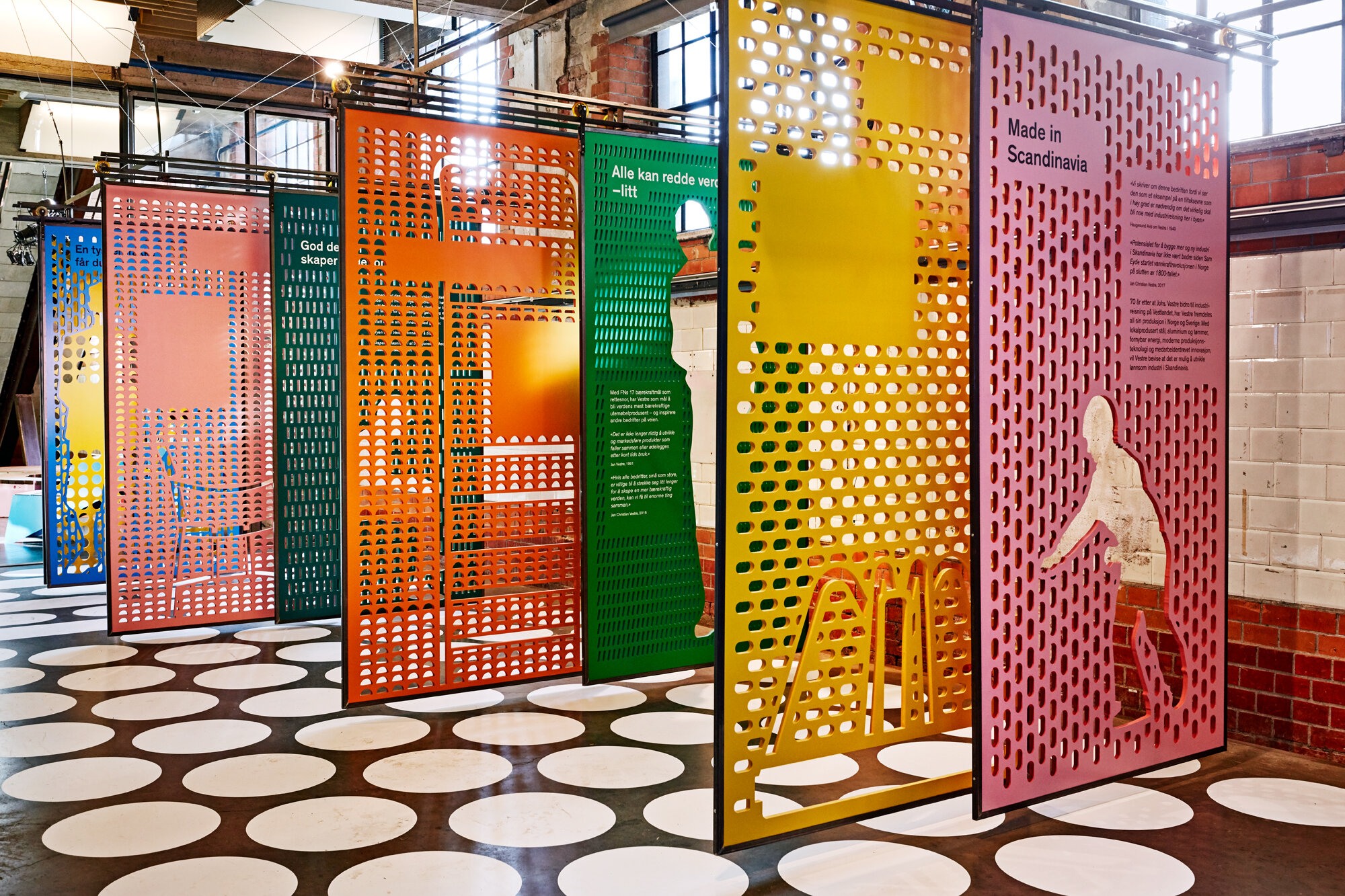 En rekke perforerte metallplater i ulike farger fungerer som utstillingsplansjer som forteller historien om møbelprodusenten vestre. Sett fra motsatt endre enn forrige bilde.