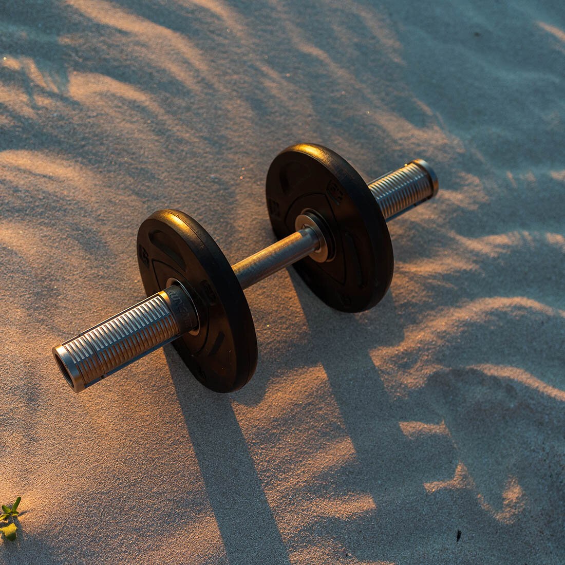 Foto av en vektstang med to vektskiver på, på sand i varmt sollys.