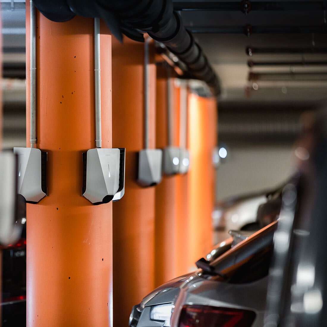 Bildet viser flere ladebokser montert på oransje pilarer i en parkeringsgarasje.